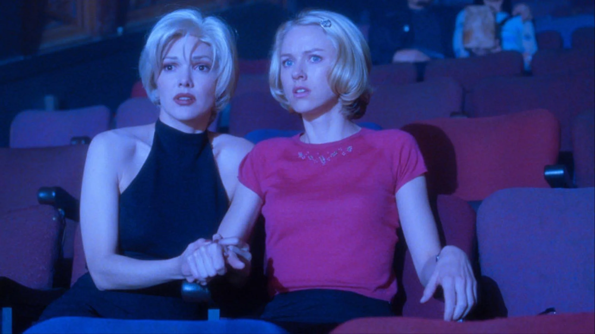 Two women sitting in a movie theater, watching a film with expressions of surprise or concern.