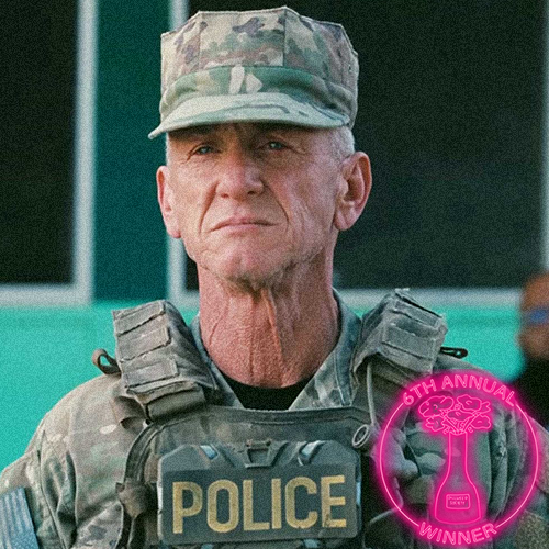 A nun with a stern expression, wearing a black habit and a white clerical collar, with a cross necklace, standing in a room with other nuns in the background.