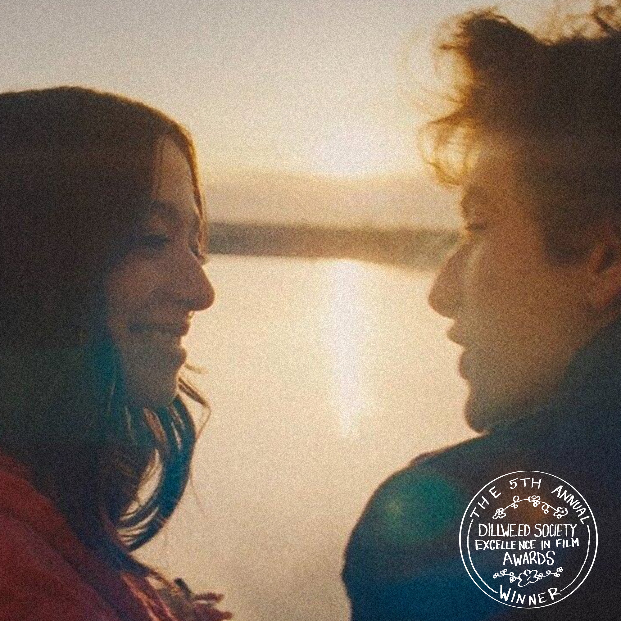 A woman and a man facing each other, smiling, with a sunset in the background. There is a circular logo in the bottom right corner that reads: 'The 5th Annual Dillweed Society Excellence in Film Awards Winner.'