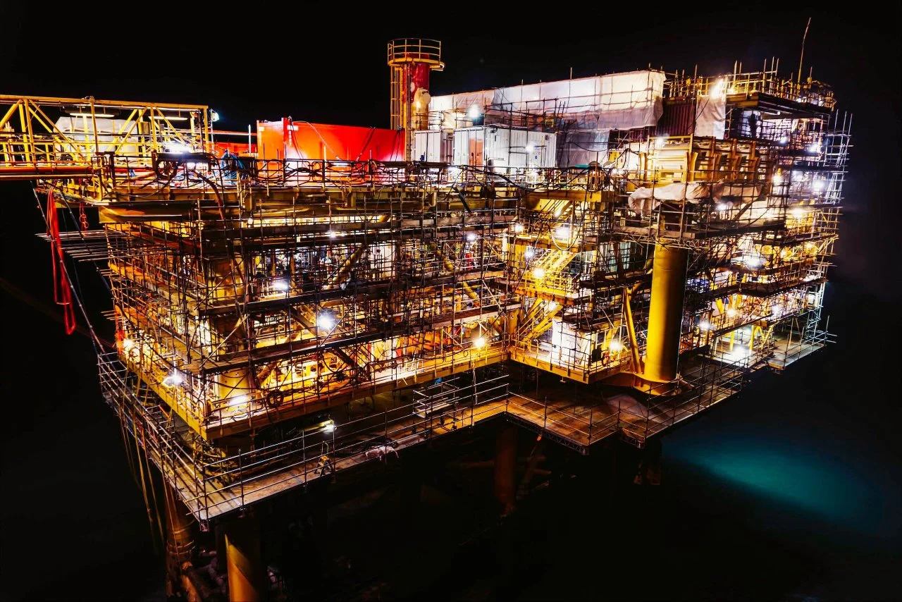 Offshore oil rig illuminated at night with lights and scaffolding.