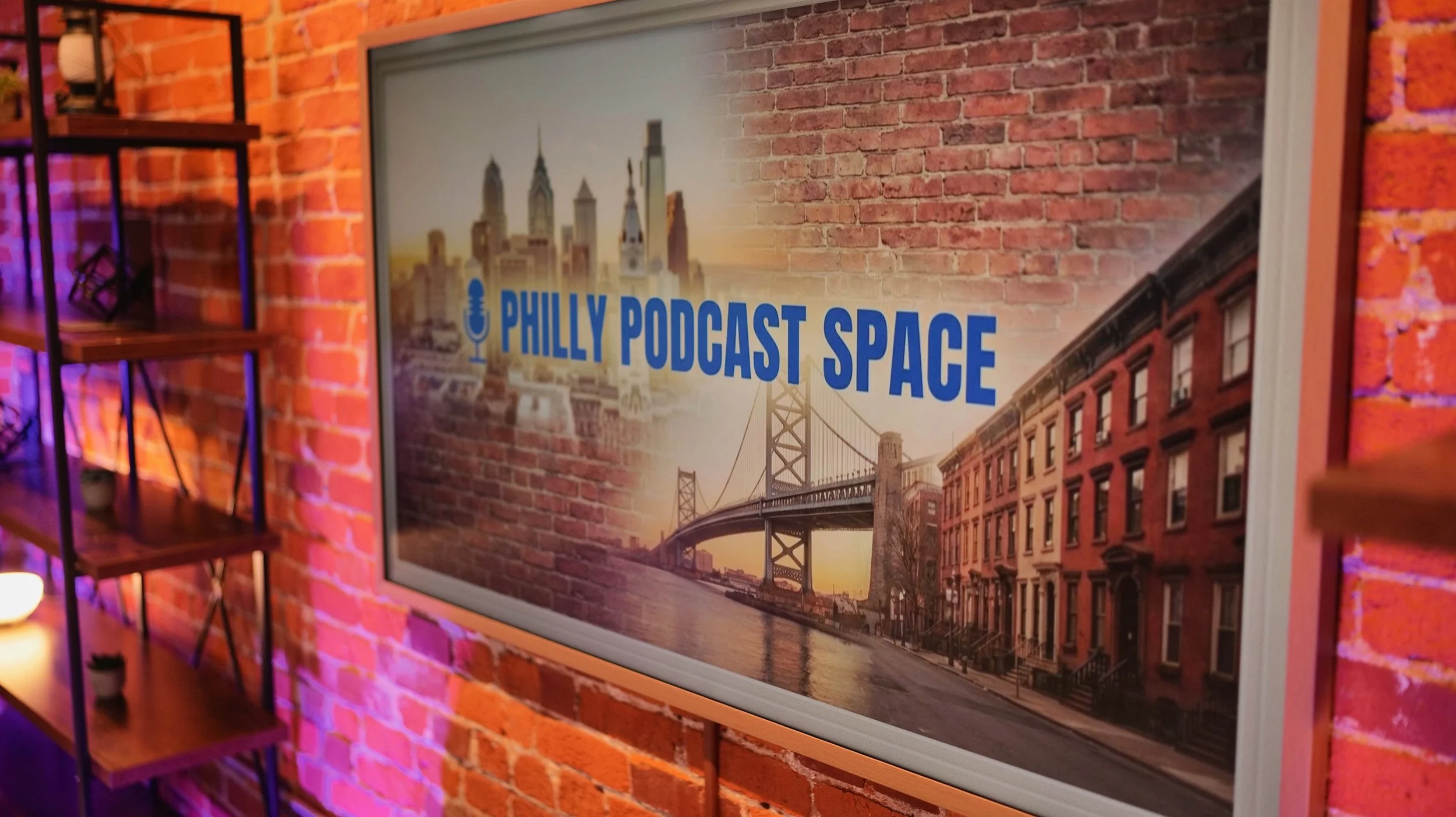 Sign reading 'Philly Podcast Space' with a background of Philadelphia city skyline and the Benjamin Franklin Bridge, mounted on an exposed brick wall.