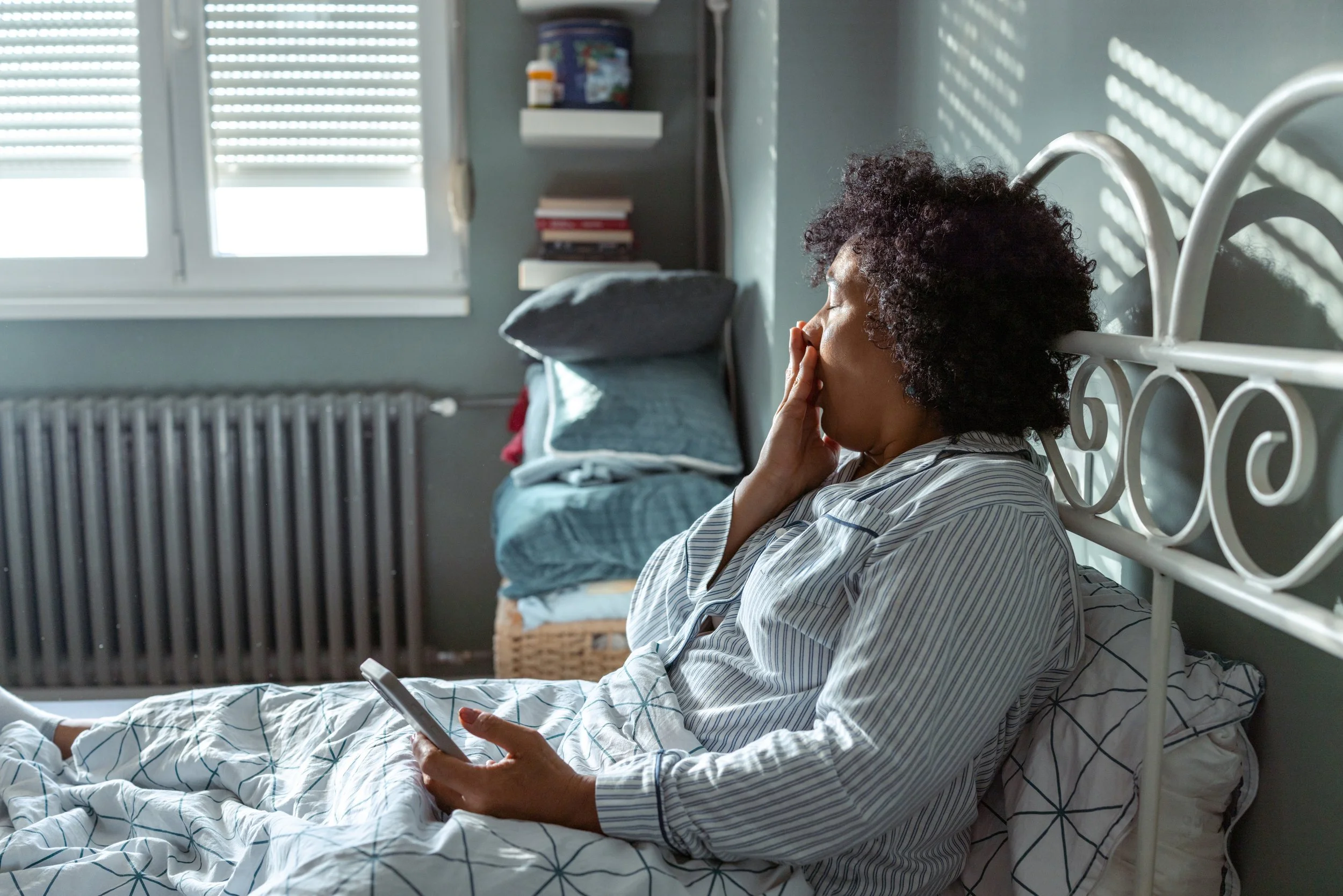 Woman sitting awake in bed and yawning.