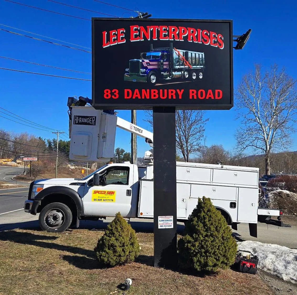 A new exterior sign for Lee Enterprises on Danbury Road - red lettering with a picture of a truck on a black background - with a Speedi Sign truck parked behind it