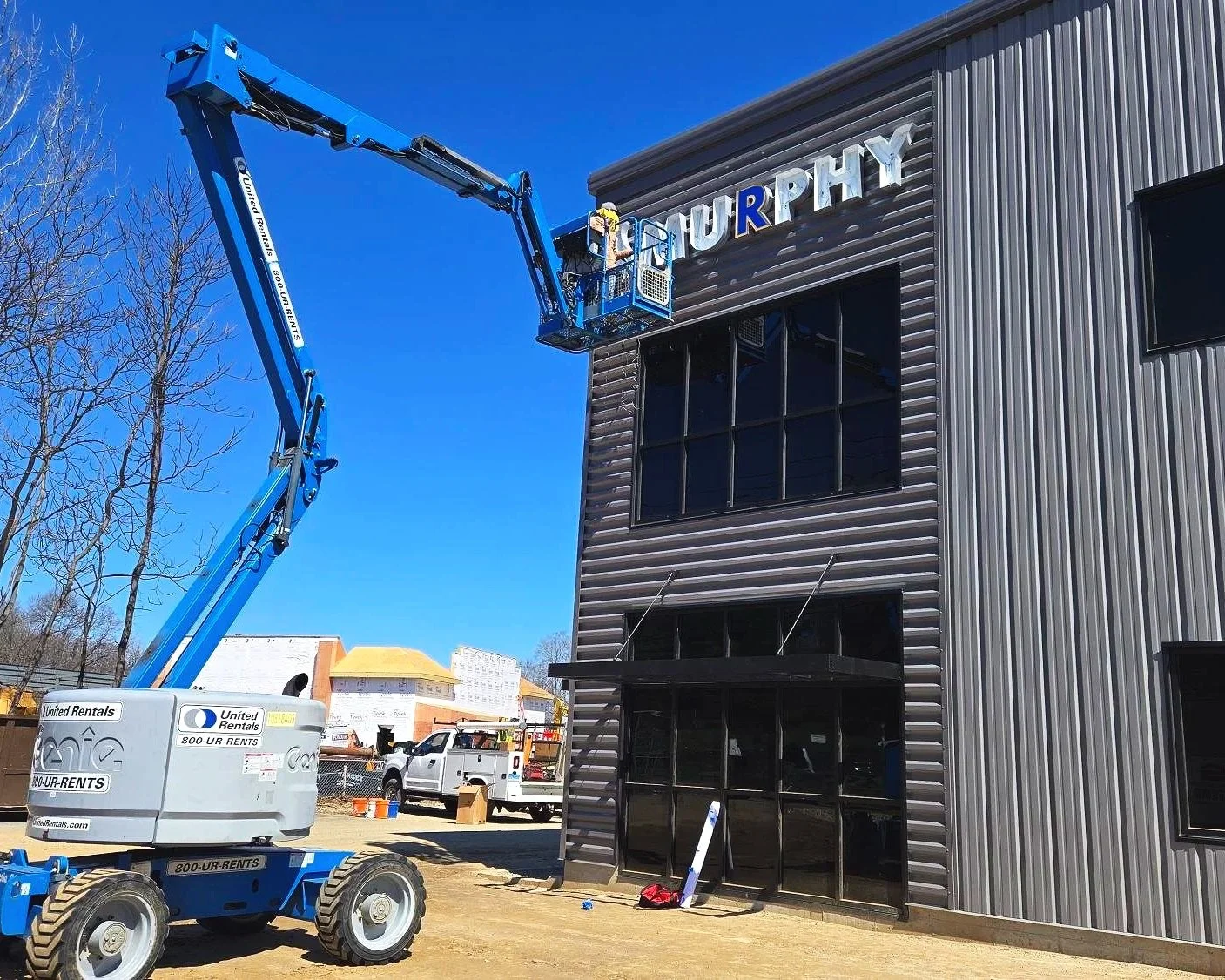 A Speedi Sign employee in a blue crane installing the Murphy Heating & Cooling sign on the outside of a grey modern building