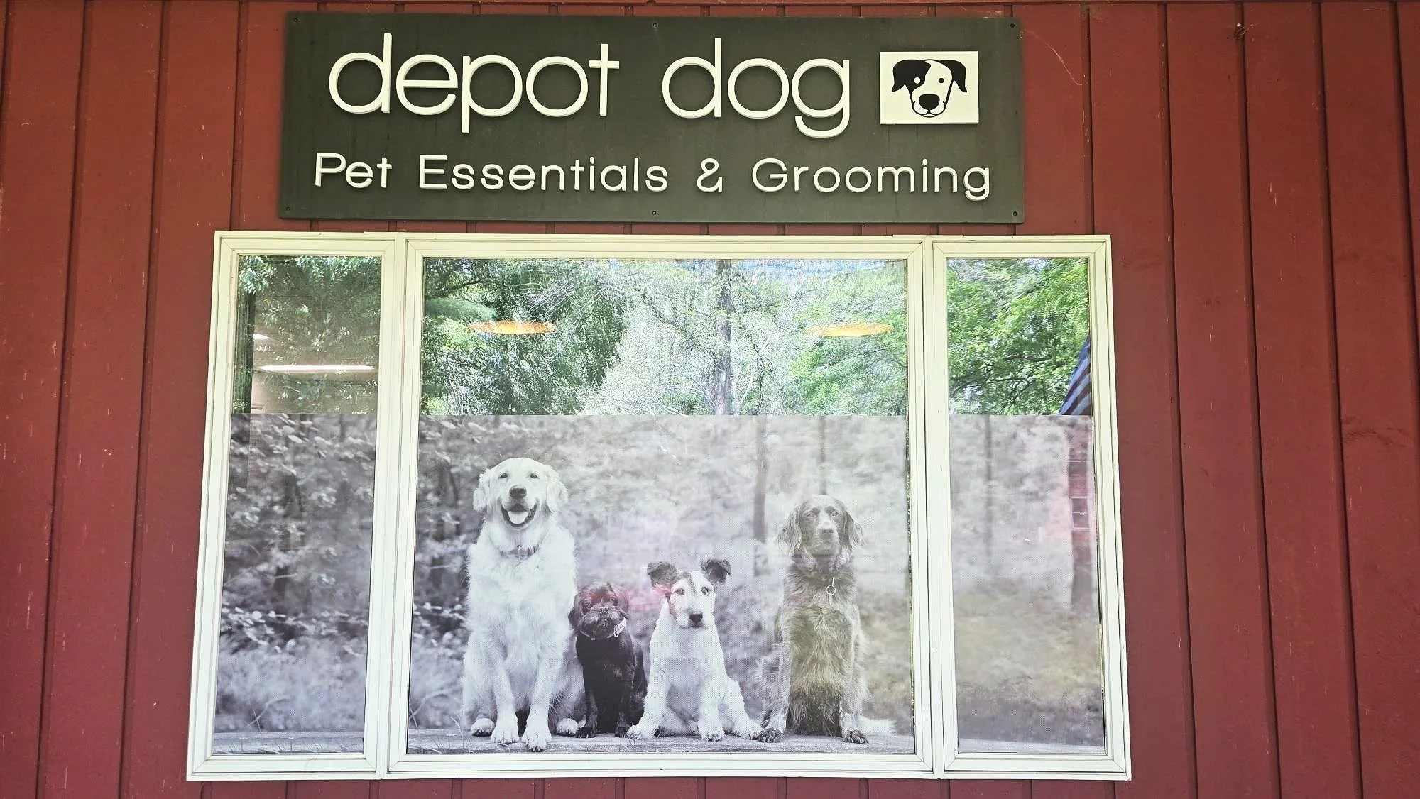 Exterior view of Depot Dog Pet Essentials & Grooming sign above a window showing a black n white photo of various dog breeds.