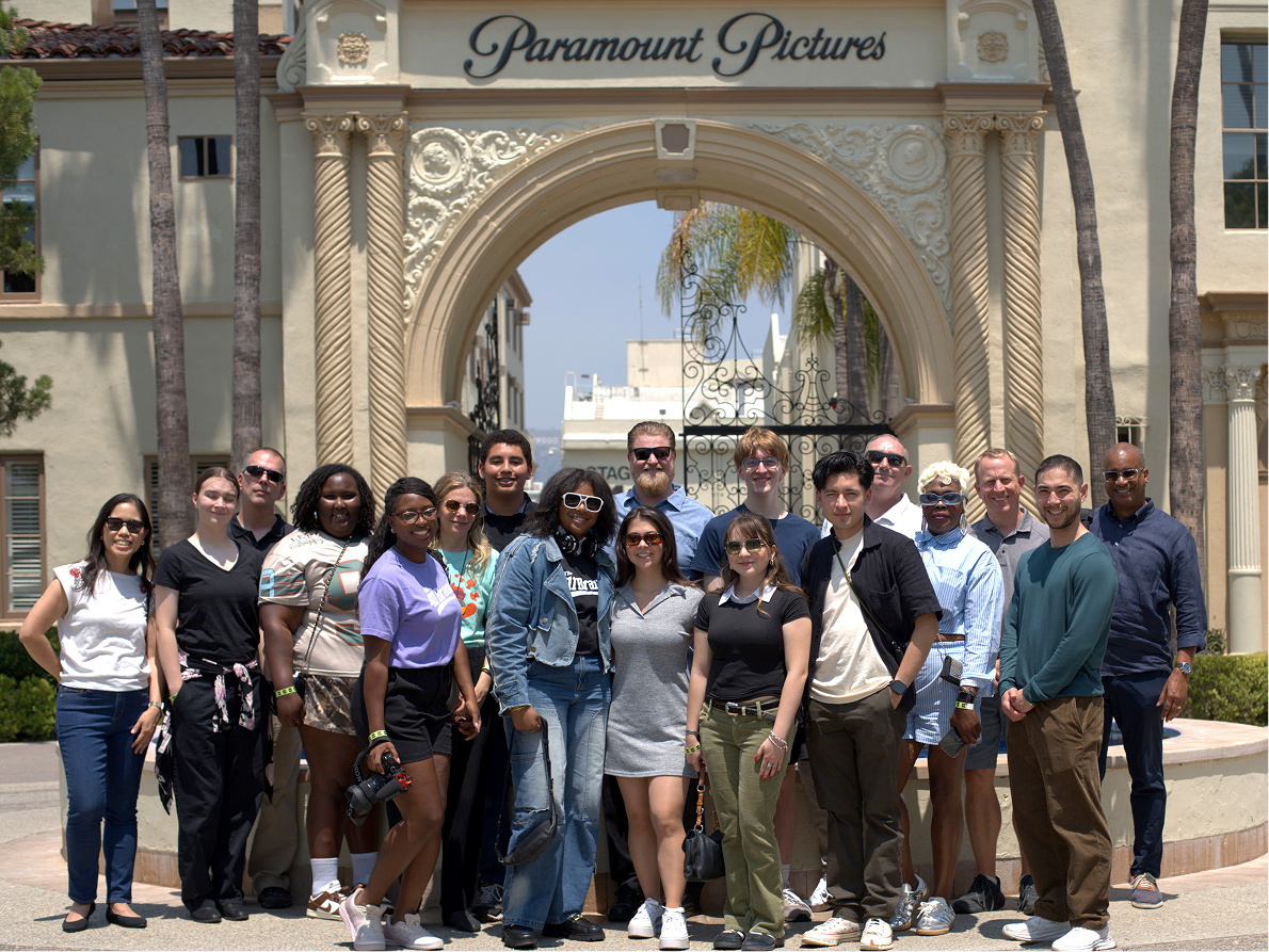 Group of people standing in front of the Paramount Pictures gate at an outdoor event.