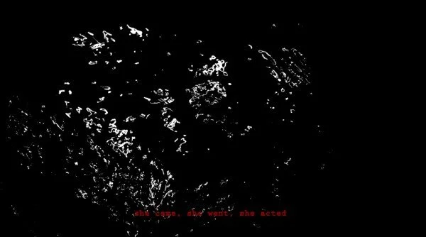 A video still of 'SHE' with a black background, abstract white shapes and red text at the bottom that reads, 'the scene, she wanted, she acted.'