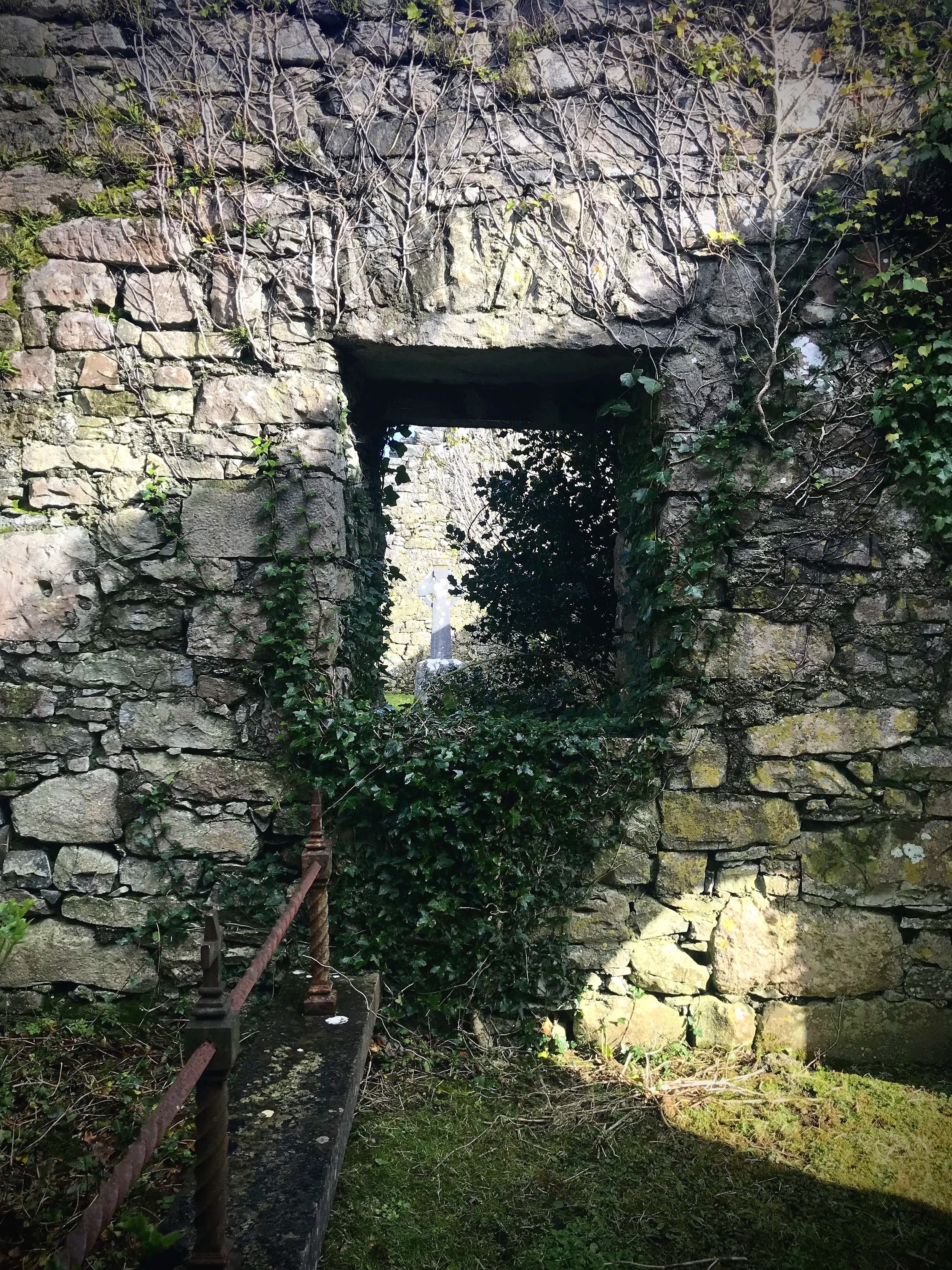 Ancient ivy covered stone wall with dark opening evoking the layered healing of scar tissue remediation and bodywork