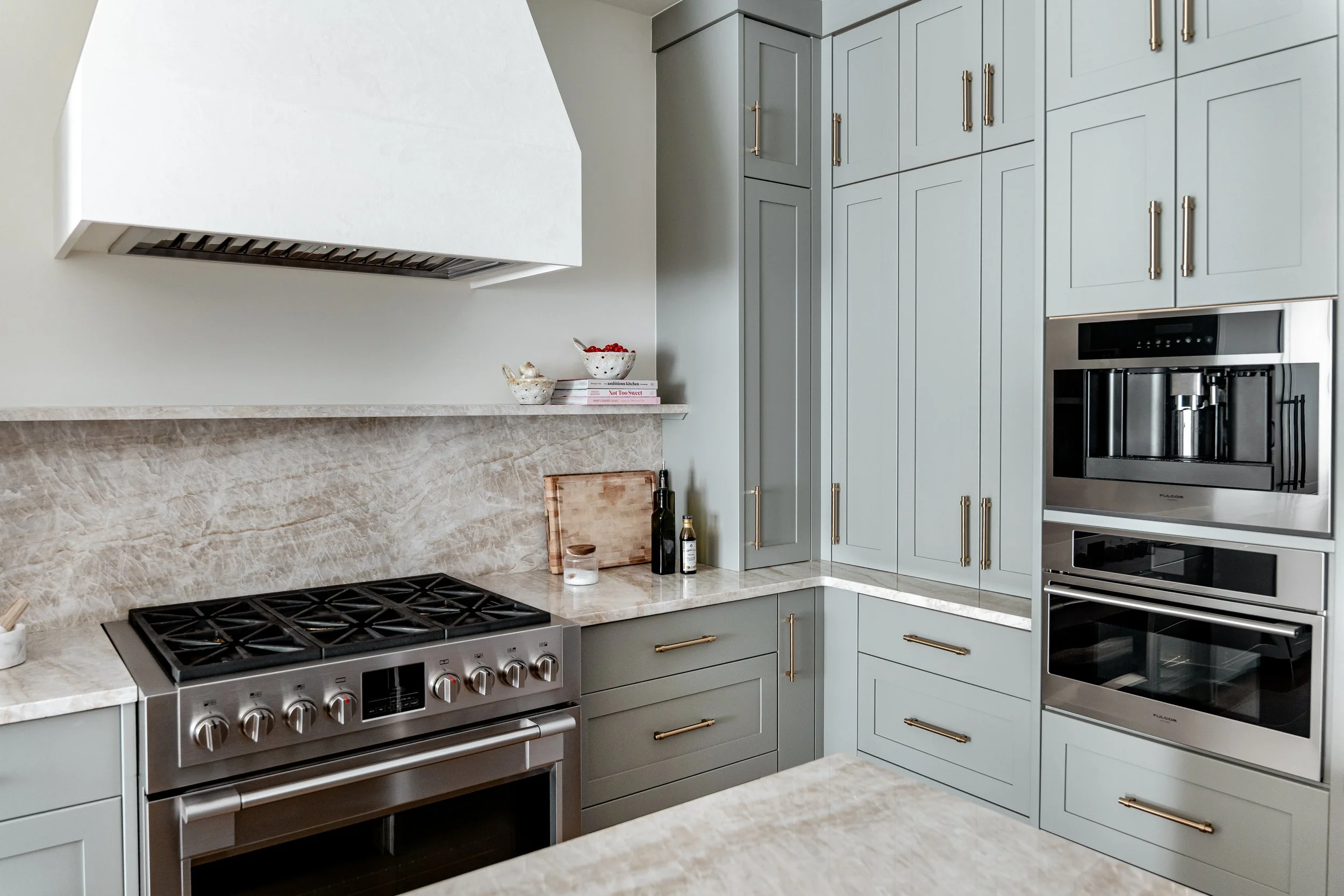 A modern kitchen with blue cabinets, stainless steel appliances, a marble countertop, a stove, and a built-in coffee maker.