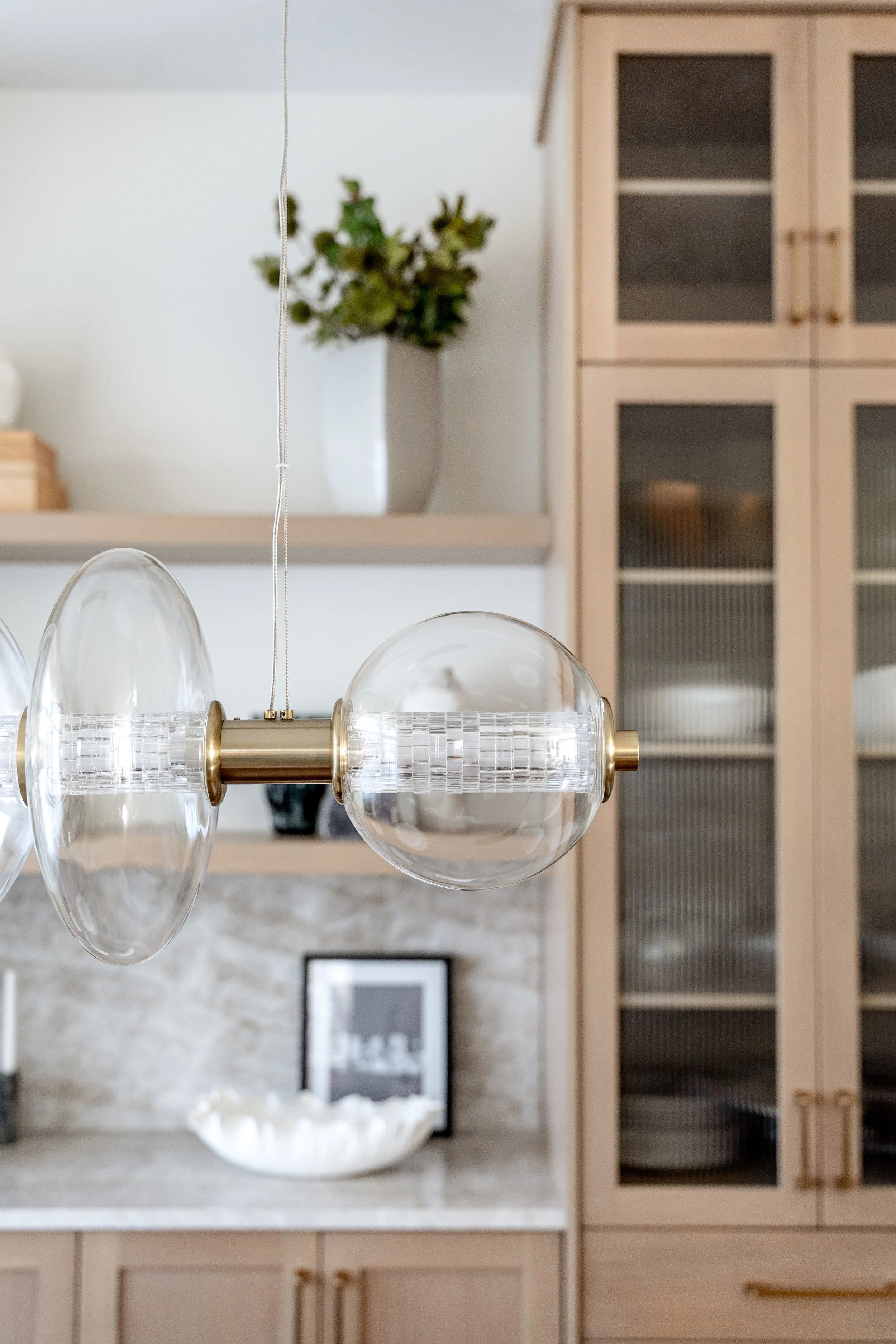 Modern kitchen with wooden cabinets, a decorative hanging light fixture, a white vase with green foliage, and a bowl of eggs on the countertop.