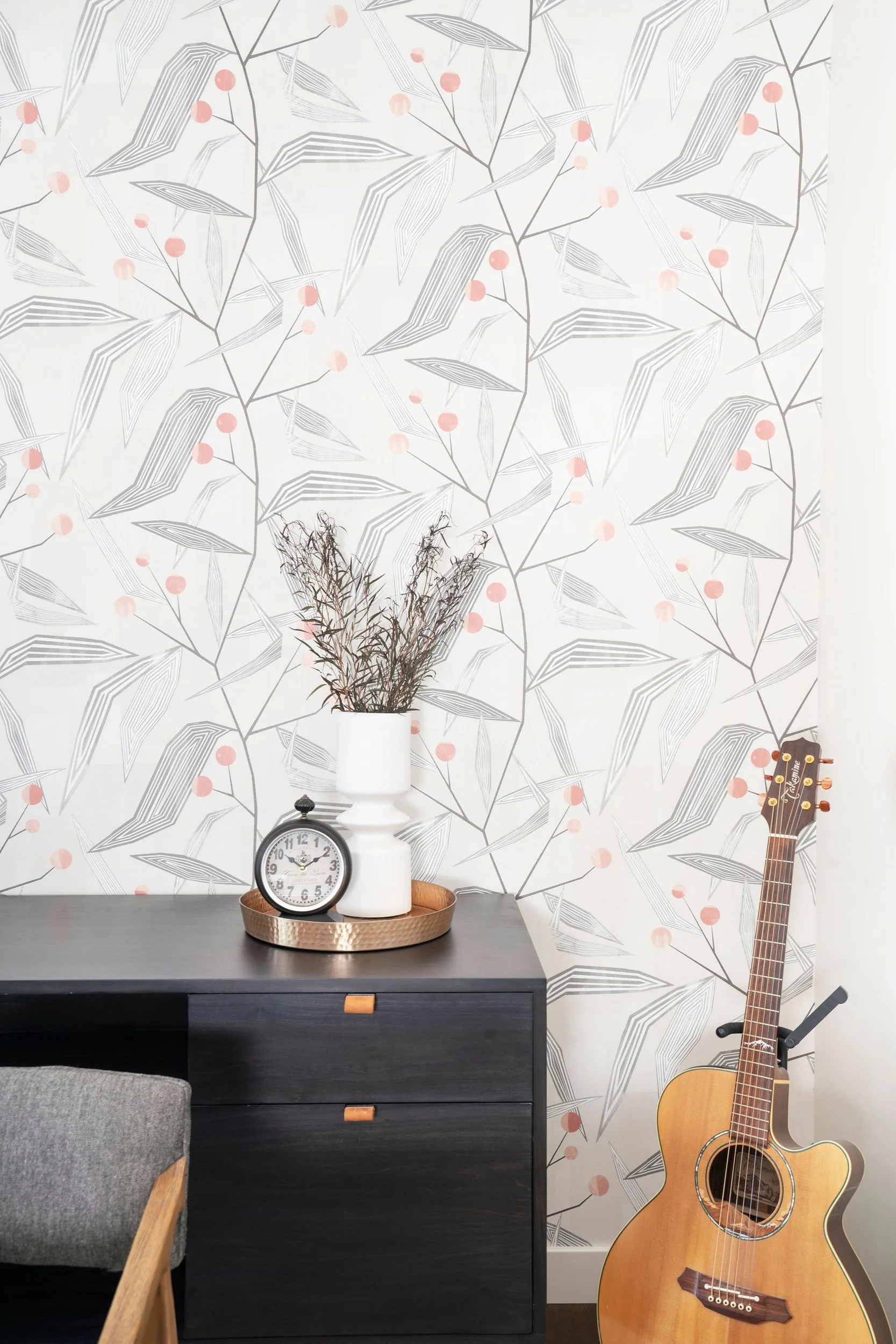 Room interior with floral wallpaper, dark wood desk, potted plant, vintage clock, guitar on stand.