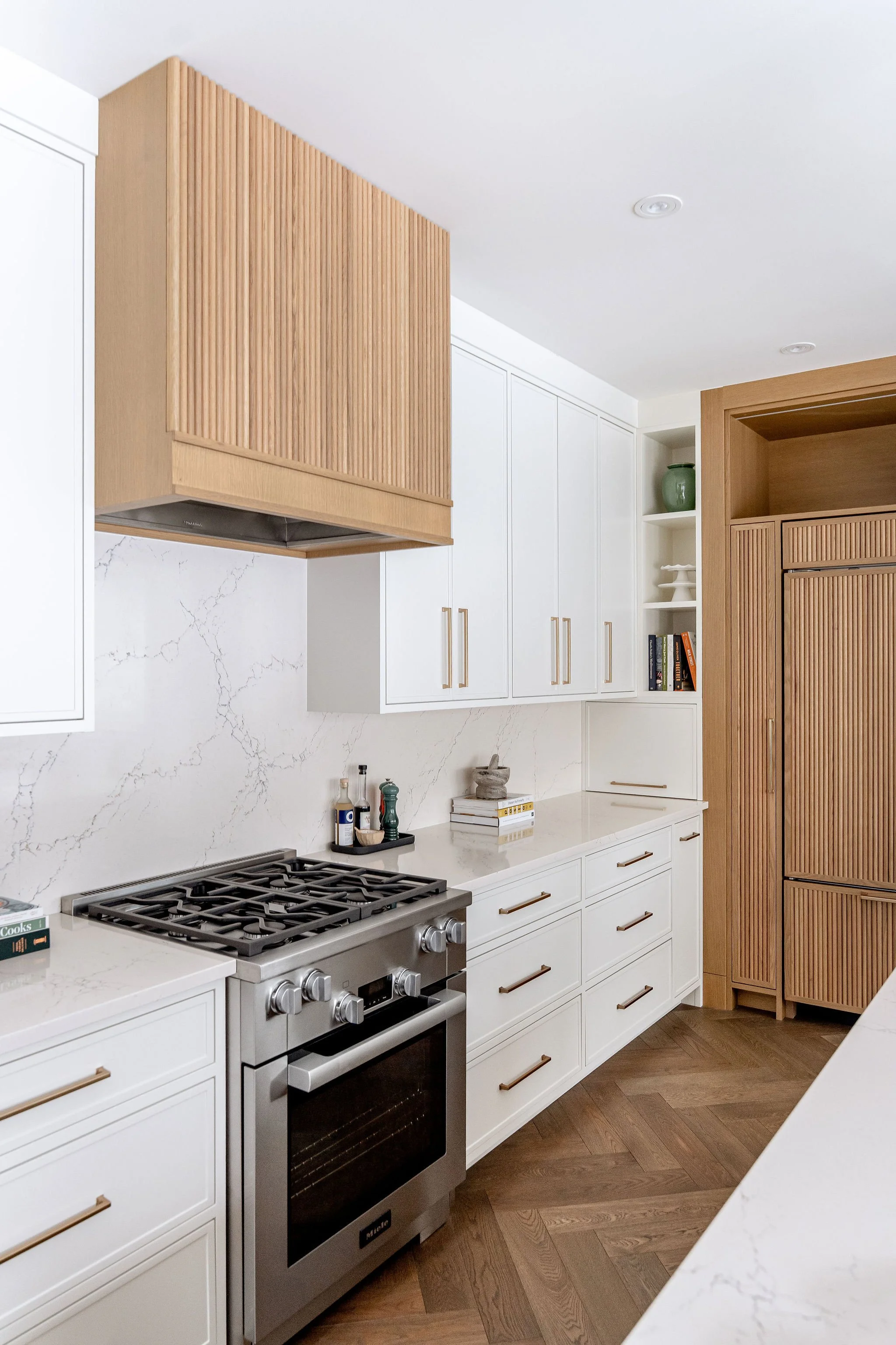 Modern kitchen with white cabinets, wooden accents, marble backsplash, stainless steel stove, and wood floors.