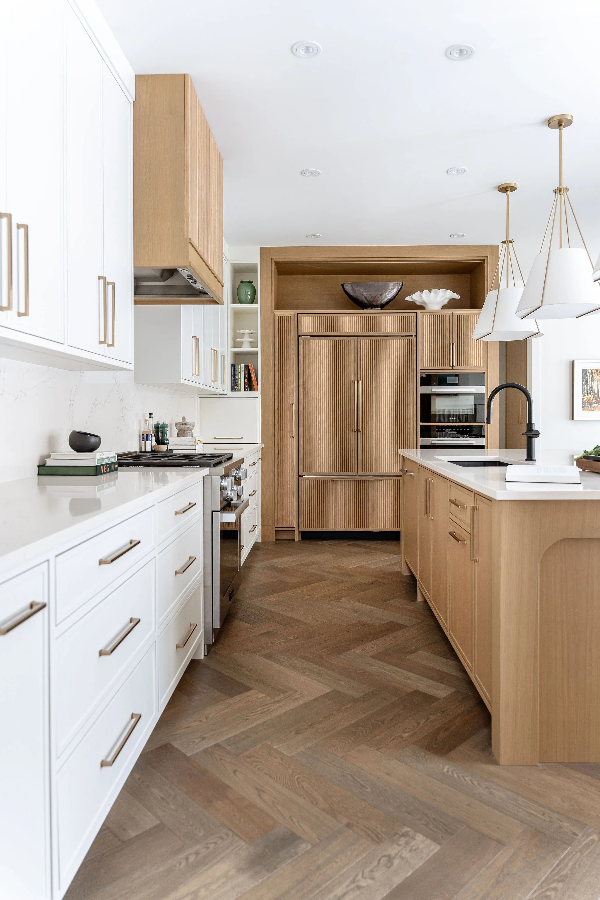 Modern kitchen with white cabinets, wooden cabinetry, marble countertops, black faucet, and decorative bowls on upper shelves.