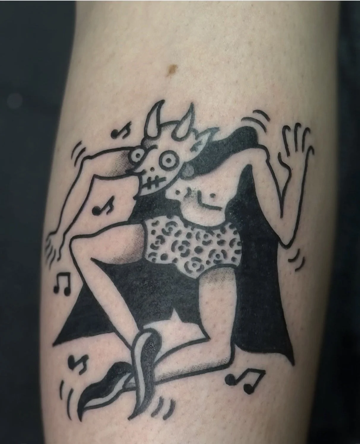 Tattoo of a woman in leopard print shorts and black cape, wearing a skeleton mask, cheering with musical notes around, in a playful and whimsical style.