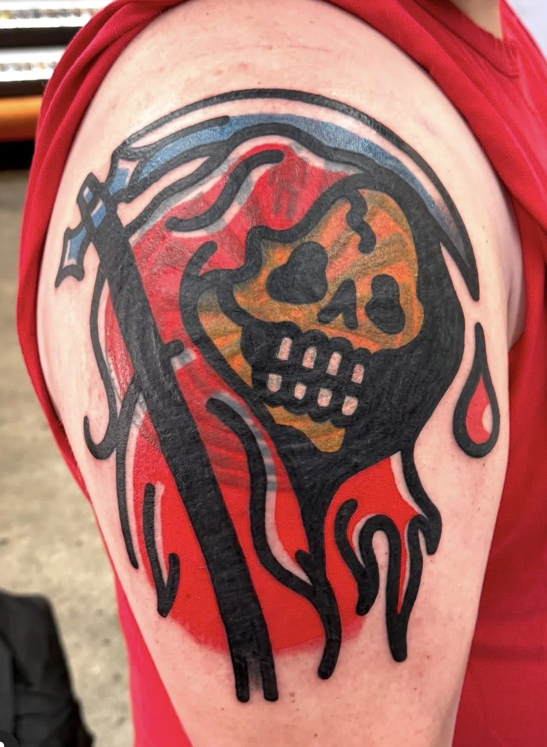 Tattoo of a skull with a bandana, with fiery details and a hood, on a person's upper arm.