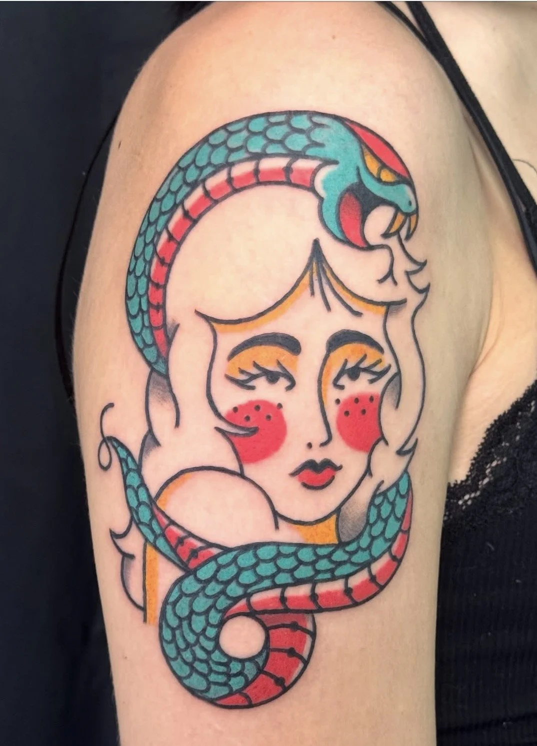 Colorful tattoo of a woman with closed eyes, red cheeks, and blonde hair, entwined with a blue and red snake on upper arm.