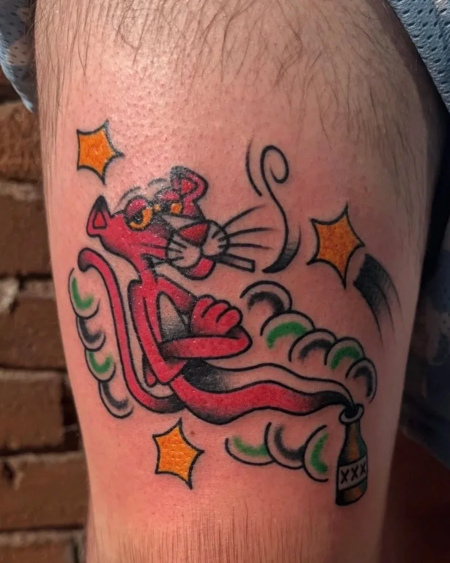 Colorful tattoo of the cartoon character Felix the Cat with a red body, sitting with crossed arms, surrounded by stars and swirls, holding a bottle.