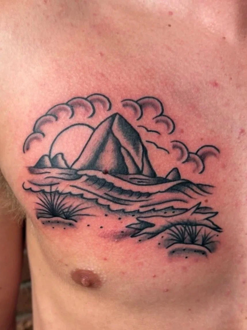 Tattoo of a mountain landscape with water, clouds, and cacti on the chest.