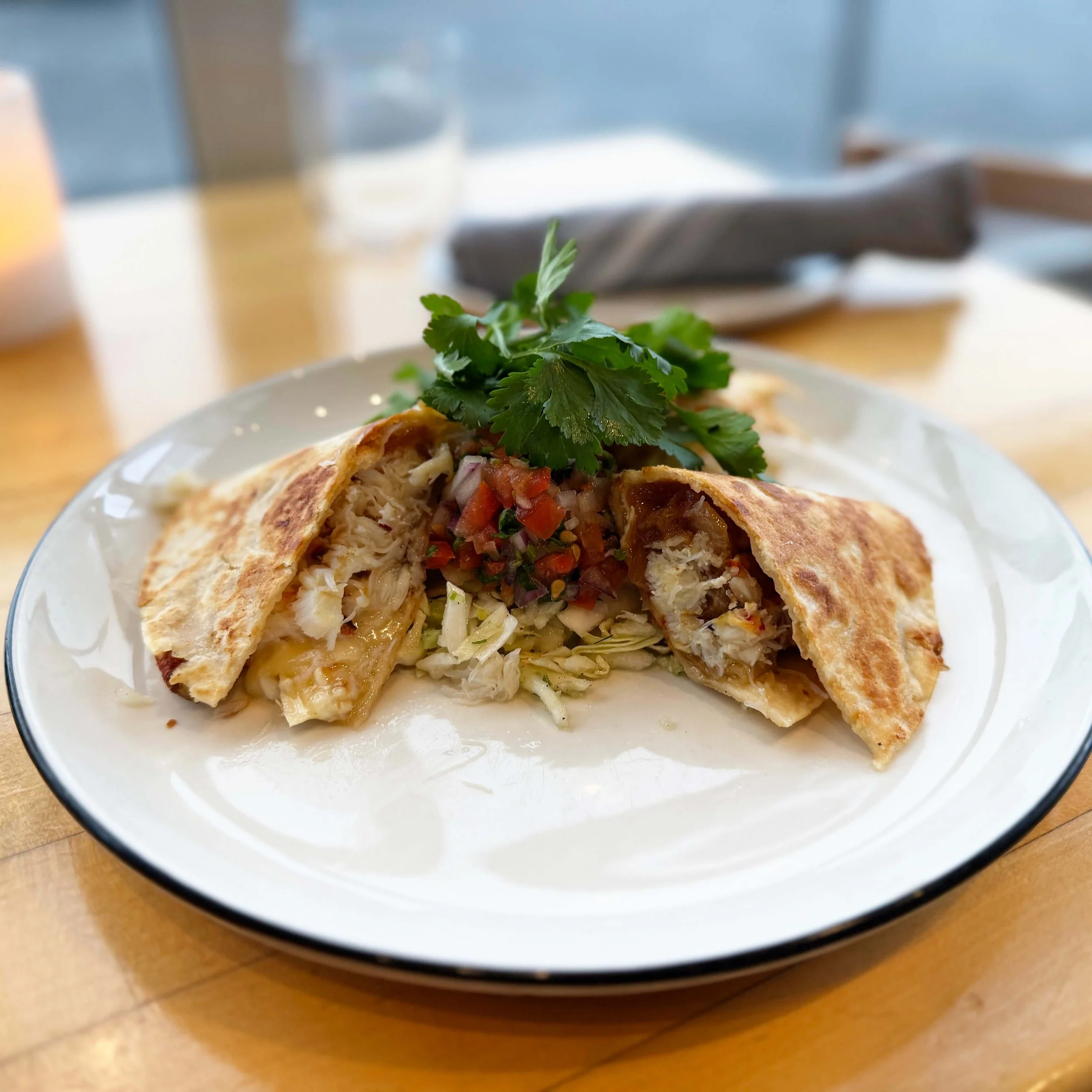 Plate with cut-in-half chicken quesadilla topped with fresh cilantro and served with shredded lettuce and tomato salsa.