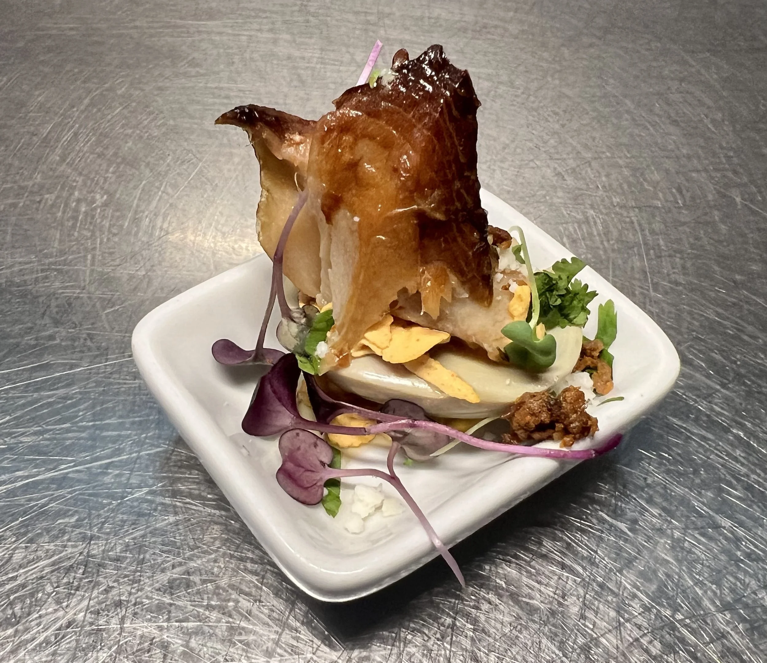 A plated portion of Black Cod fish, garnished with microgreens and sliced hard-boiled eggs on a white square dish.