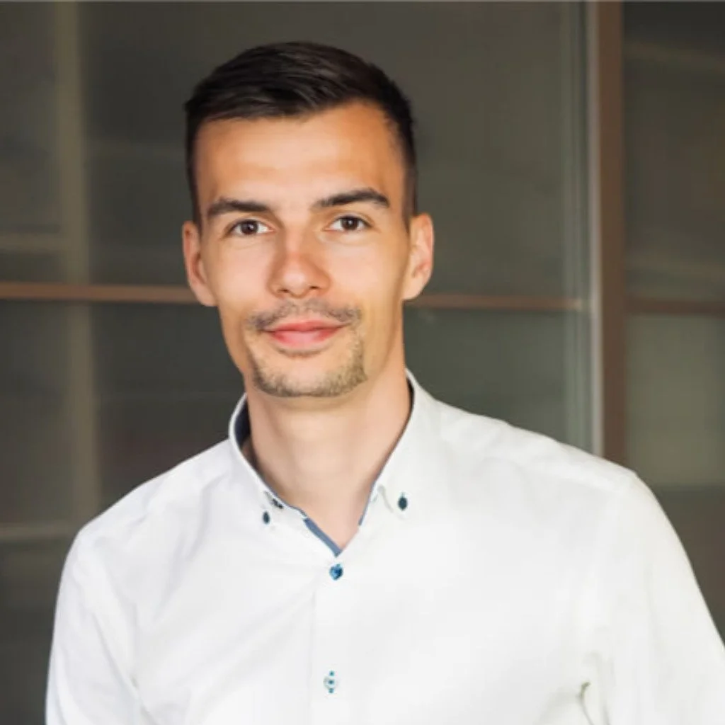 Benjamin Damm, Gründer von Treno Finance mit kurzem Haar und Schnurrbart trägt ein weißes Hemd und lächelt in die Kamera.