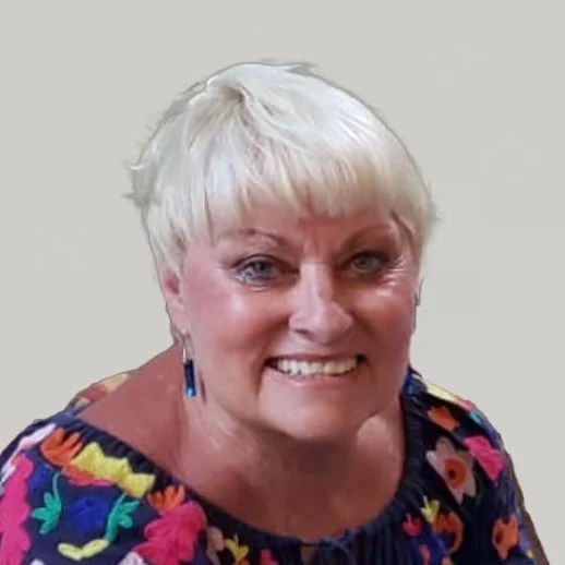 Ältere Frau mit kurzen, weißen Haaren und bunter Kleidung, die lächelt.