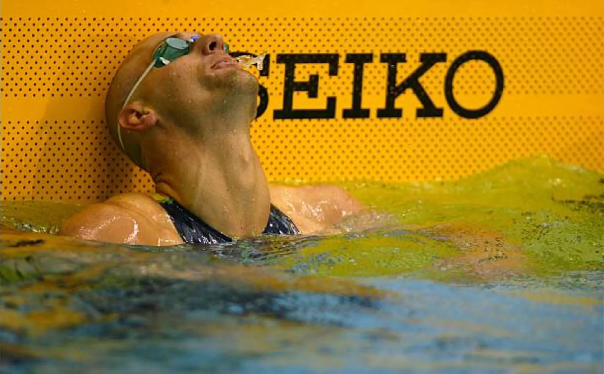 Swimmer wearing goggles resting against a yellow background with black text.