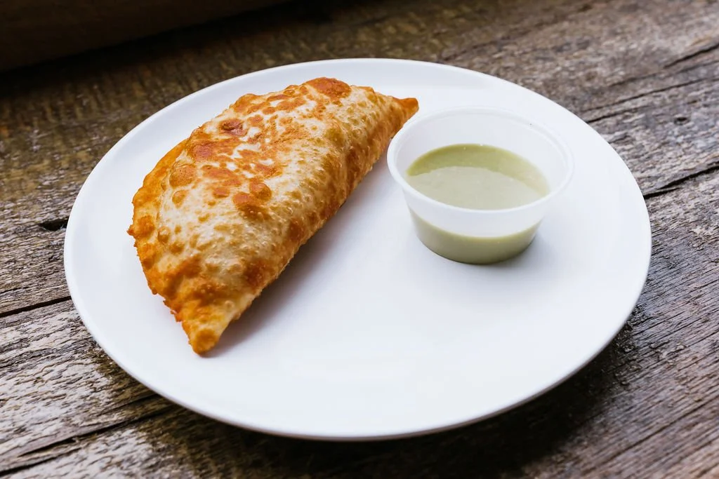 Fried empanada with a side of green dipping sauce on a white plate