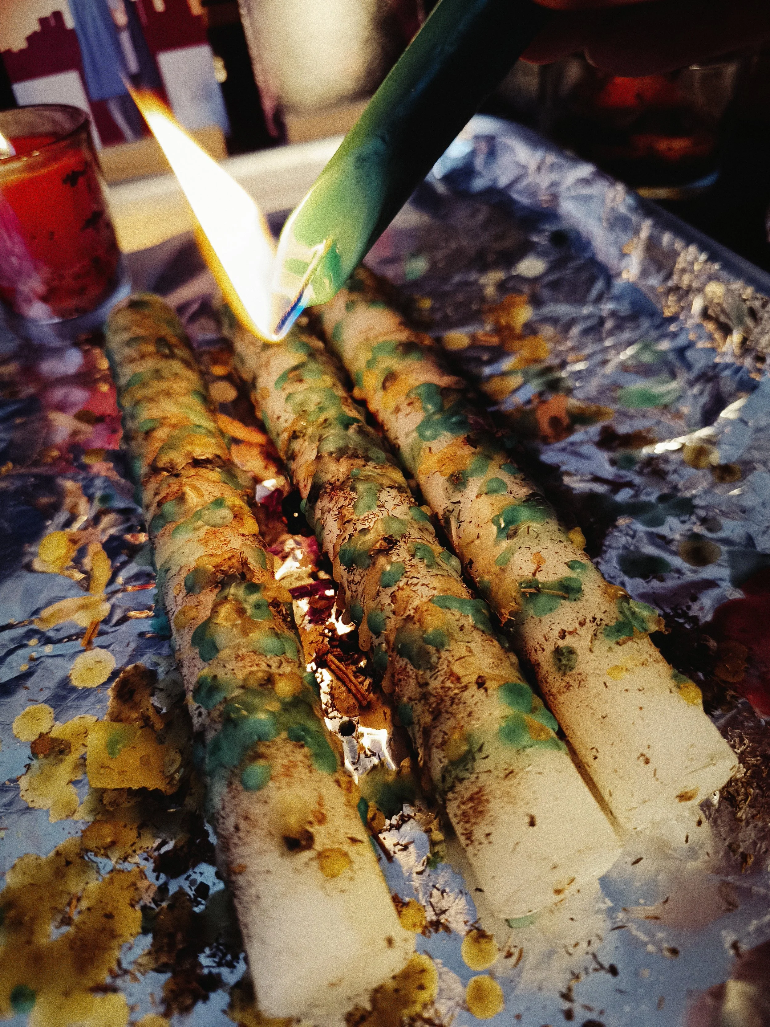Green spelled candle wax being hand-dripped onto herb-dressed white prosperity taper candles