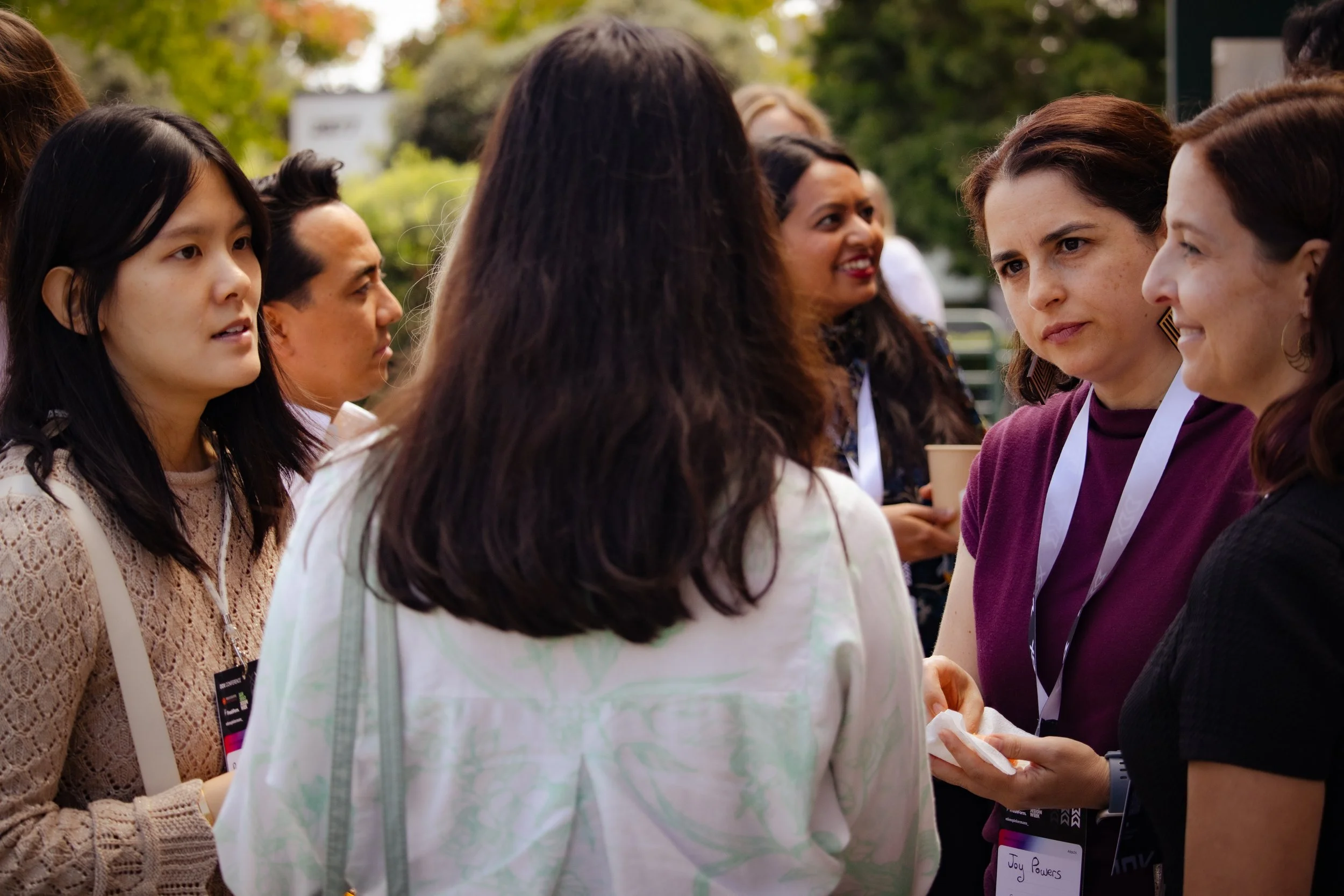 A group of diverse people engaging in a conversation outdoors, wearing conference badges.