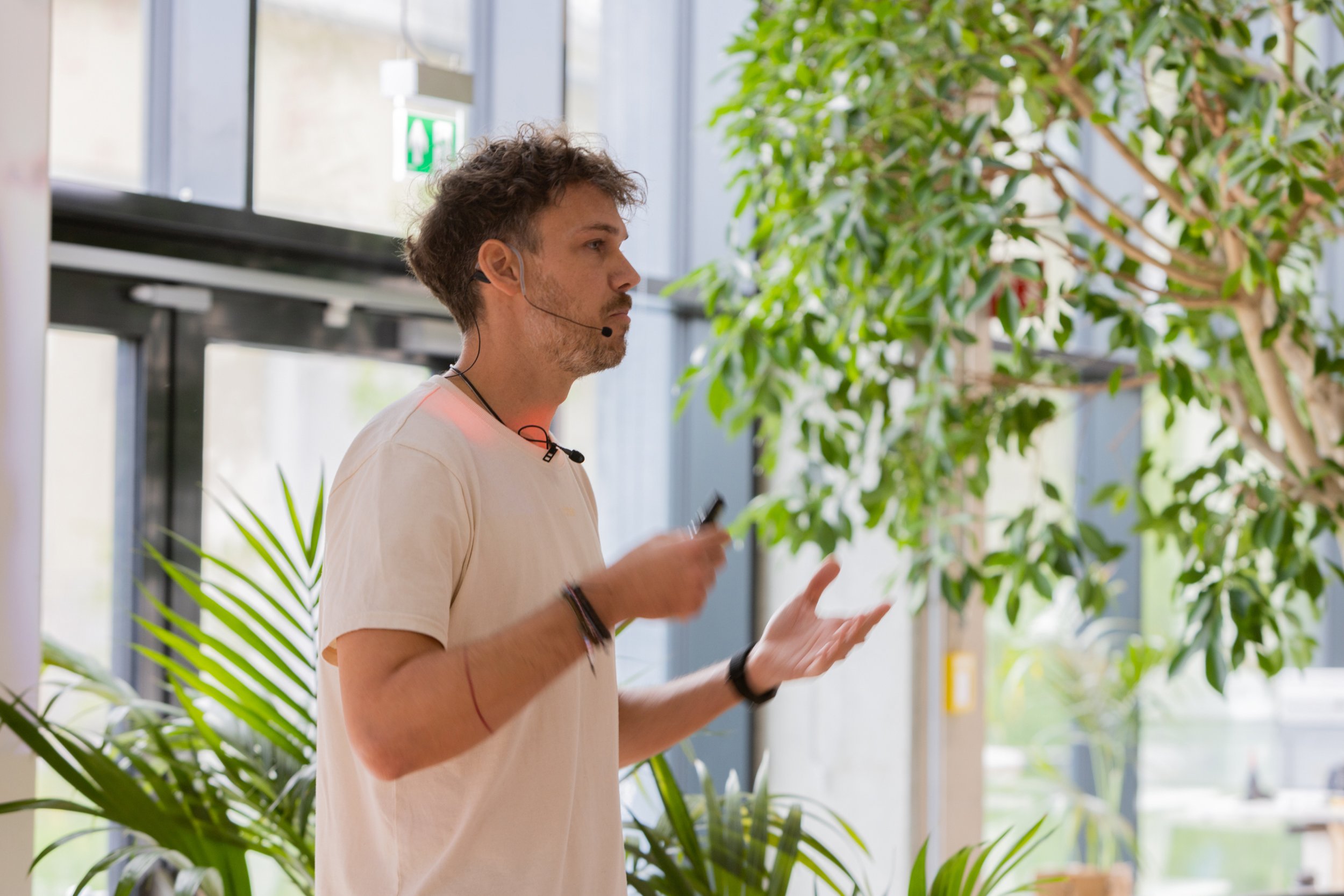Person giving a presentation indoors with a microphone, surrounded by plants.