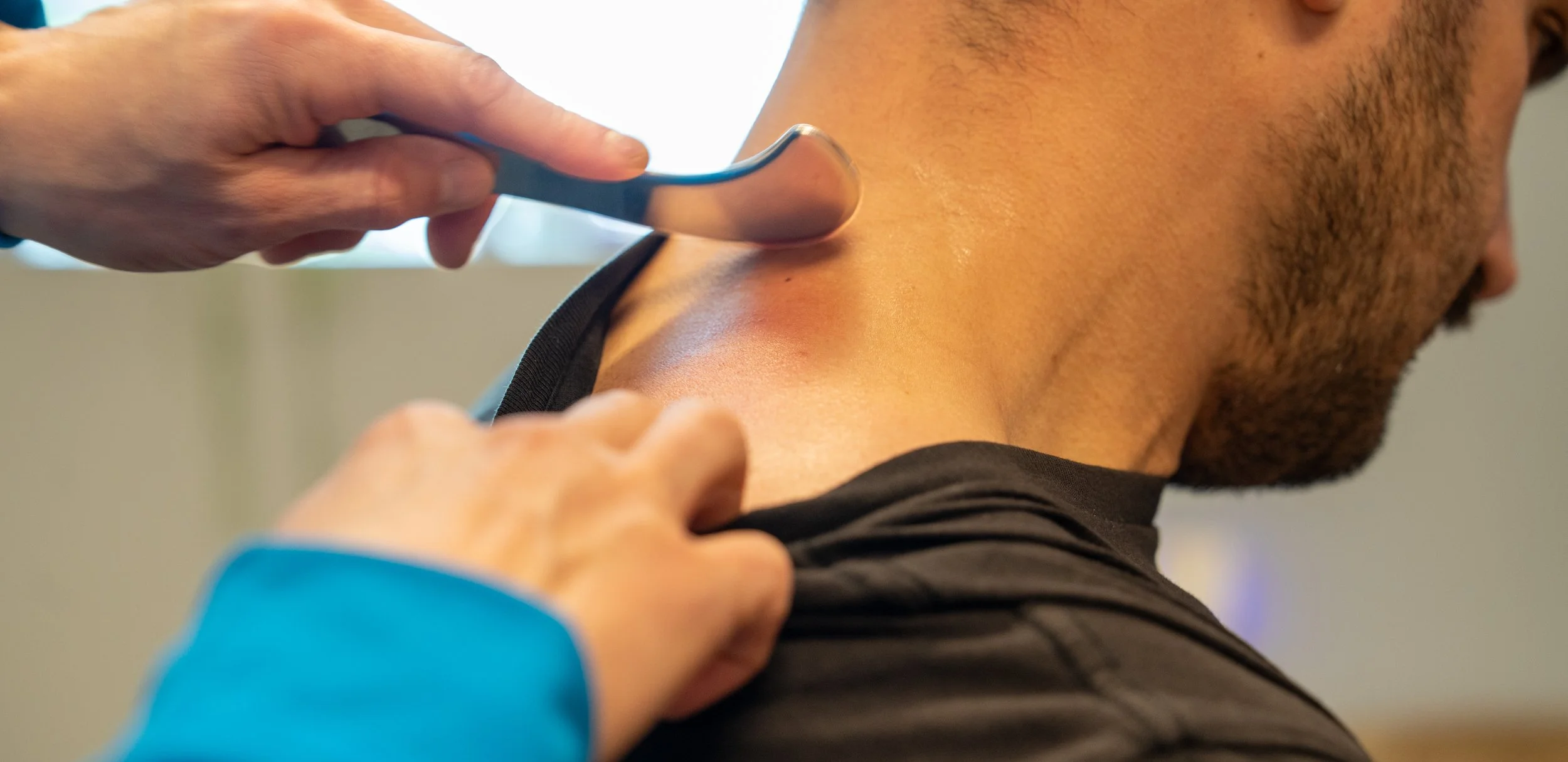 Chiropractor adjusting a patient's back in an office with a framed diploma, a computer, and anatomical posters on the wall.