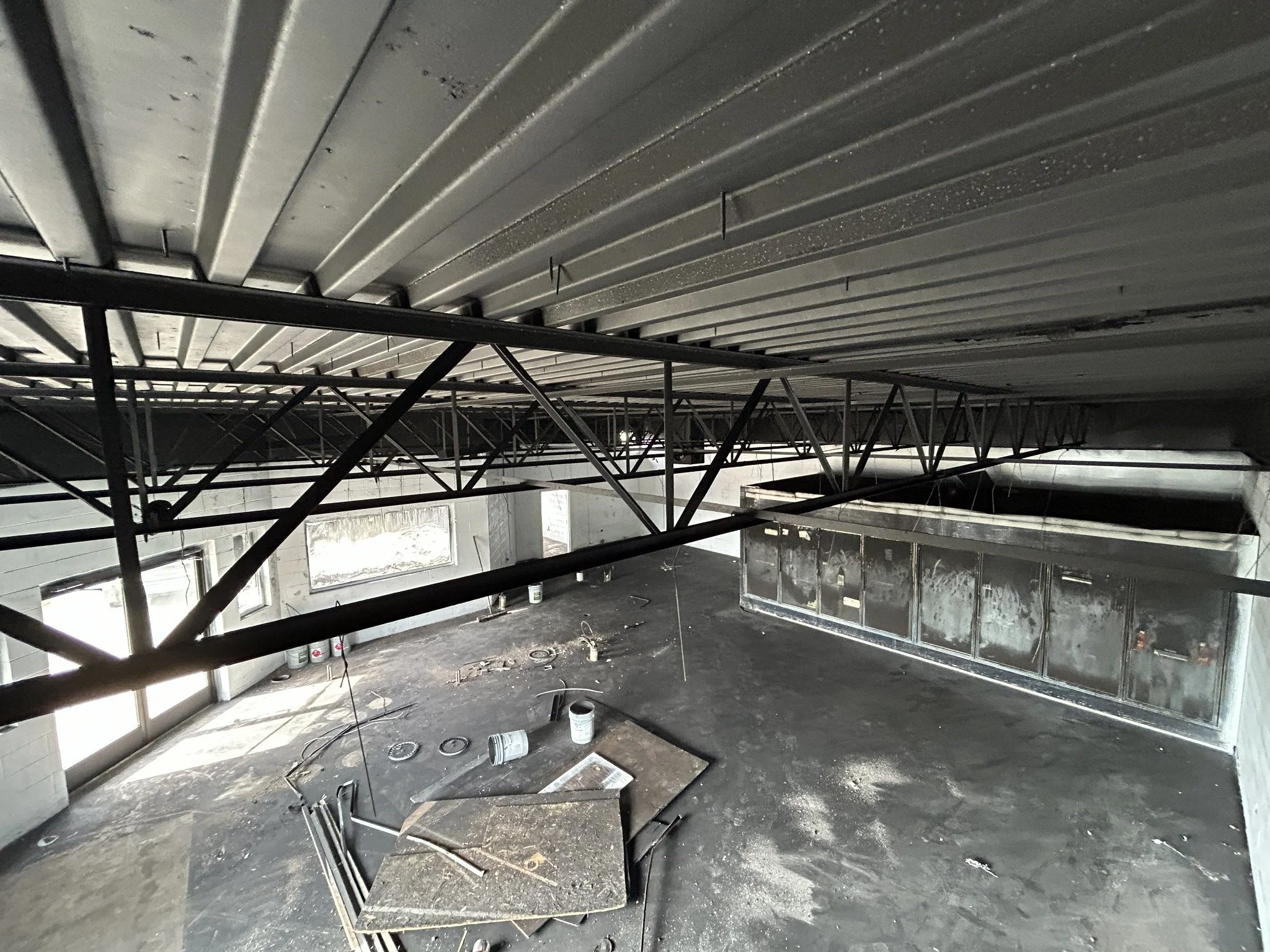 Construction site interior with metal framework, window openings, scattered tools, and supplies.