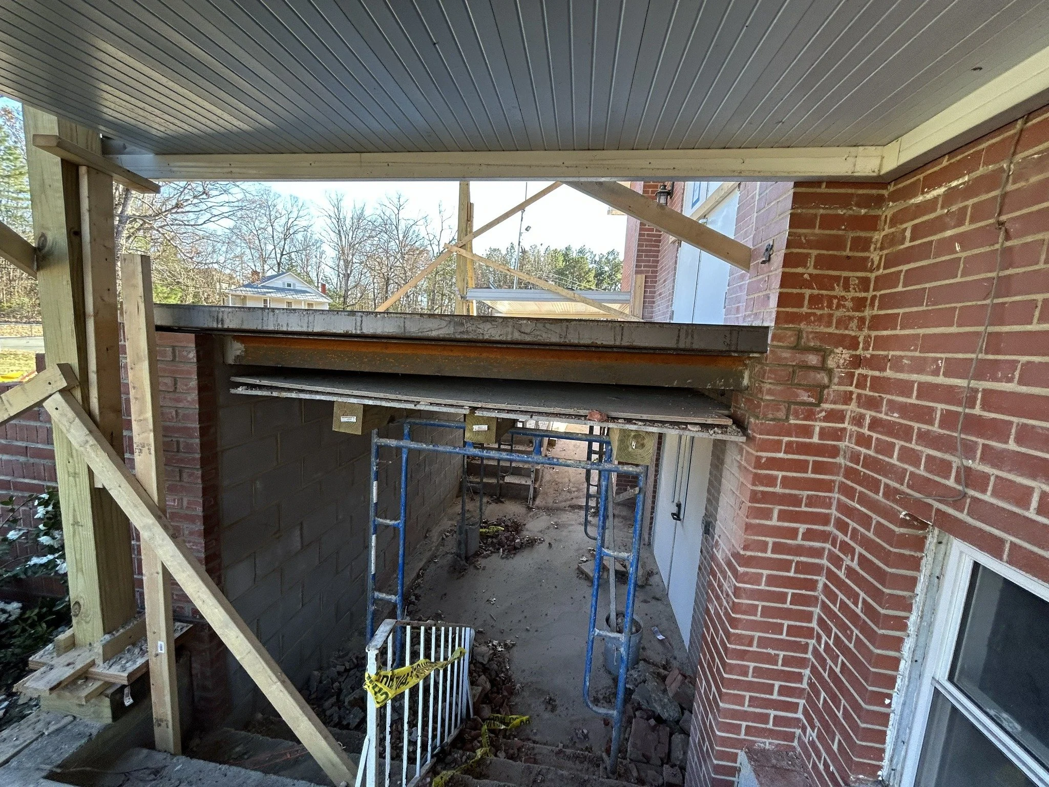 Construction site with scaffolding and wooden supports on a brick house exterior during renovation.