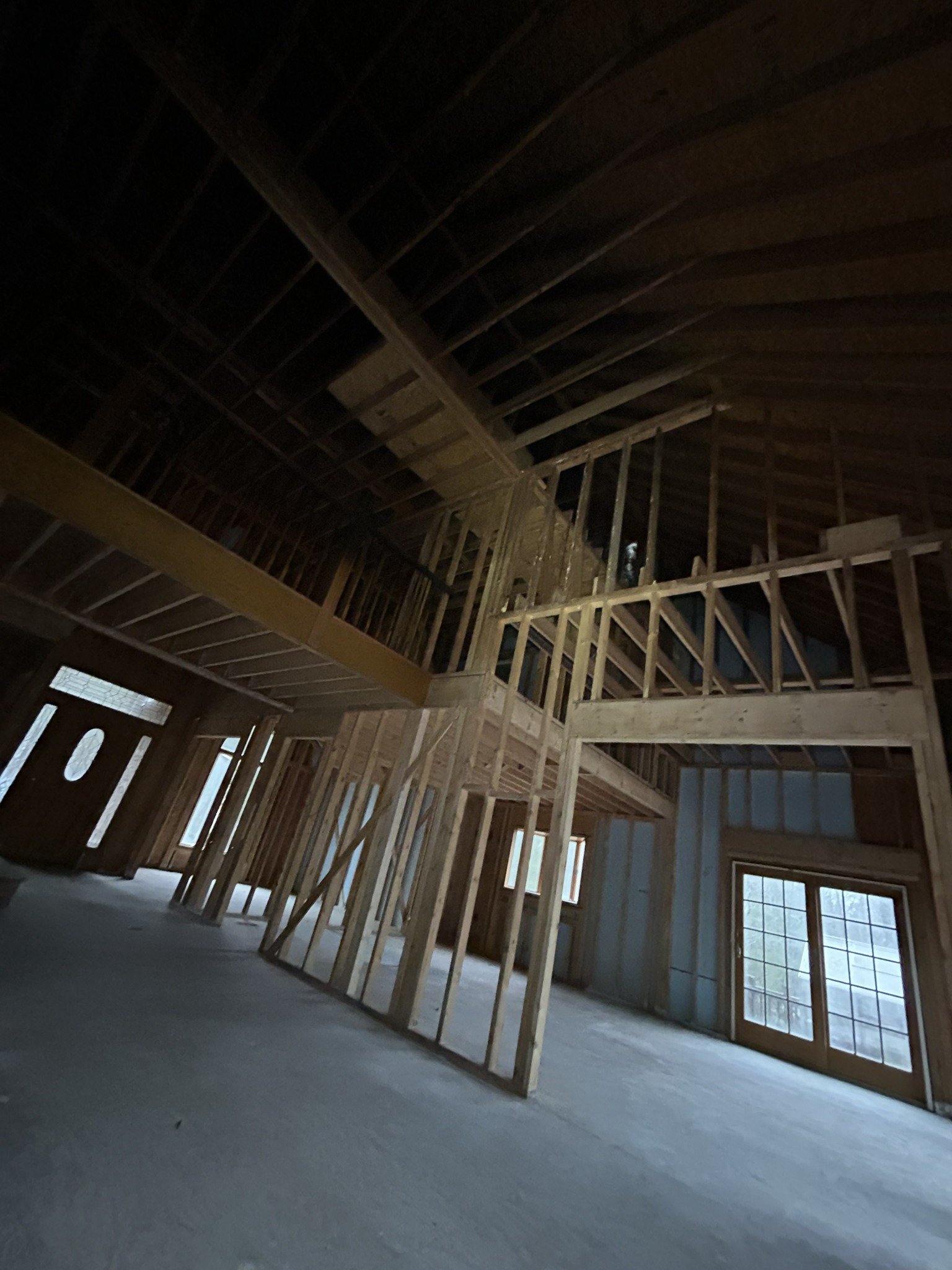 Interior view of a house under construction, showing wooden framing, window, door, and unfinished floors.
