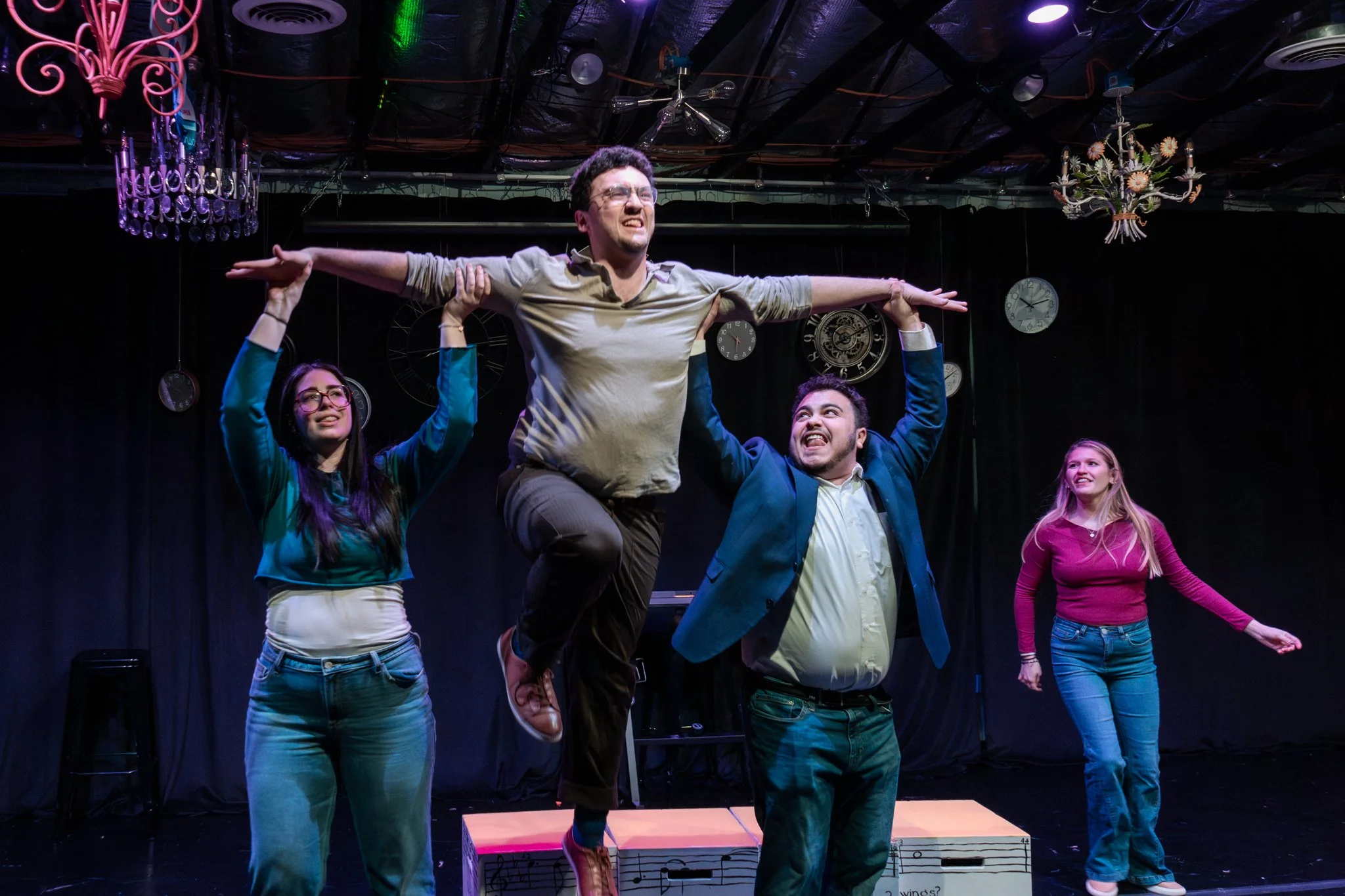 The cast of tick, tick…BOOM! mid-number under hanging chandeliers, one actor leaping at center