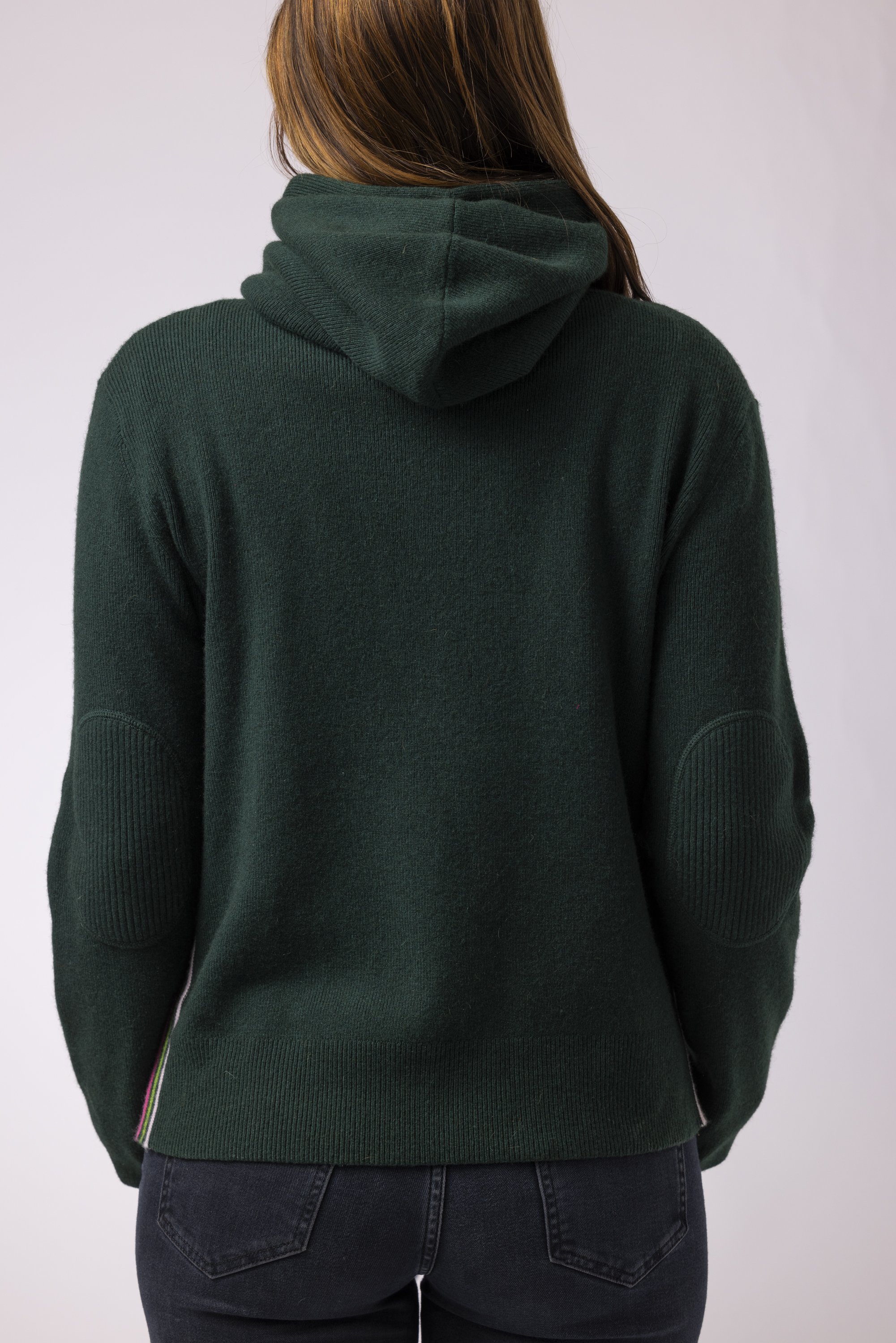 Woman in a studio wearing a dark green cashmere hoodie with retro stripes on sides facing backside