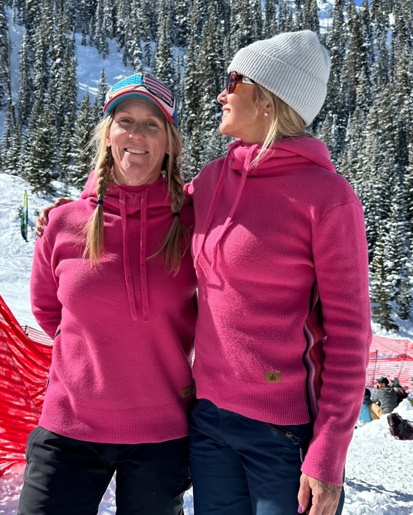 Two women outdoors in the snow both wearing a bright pink cashmere hoodie