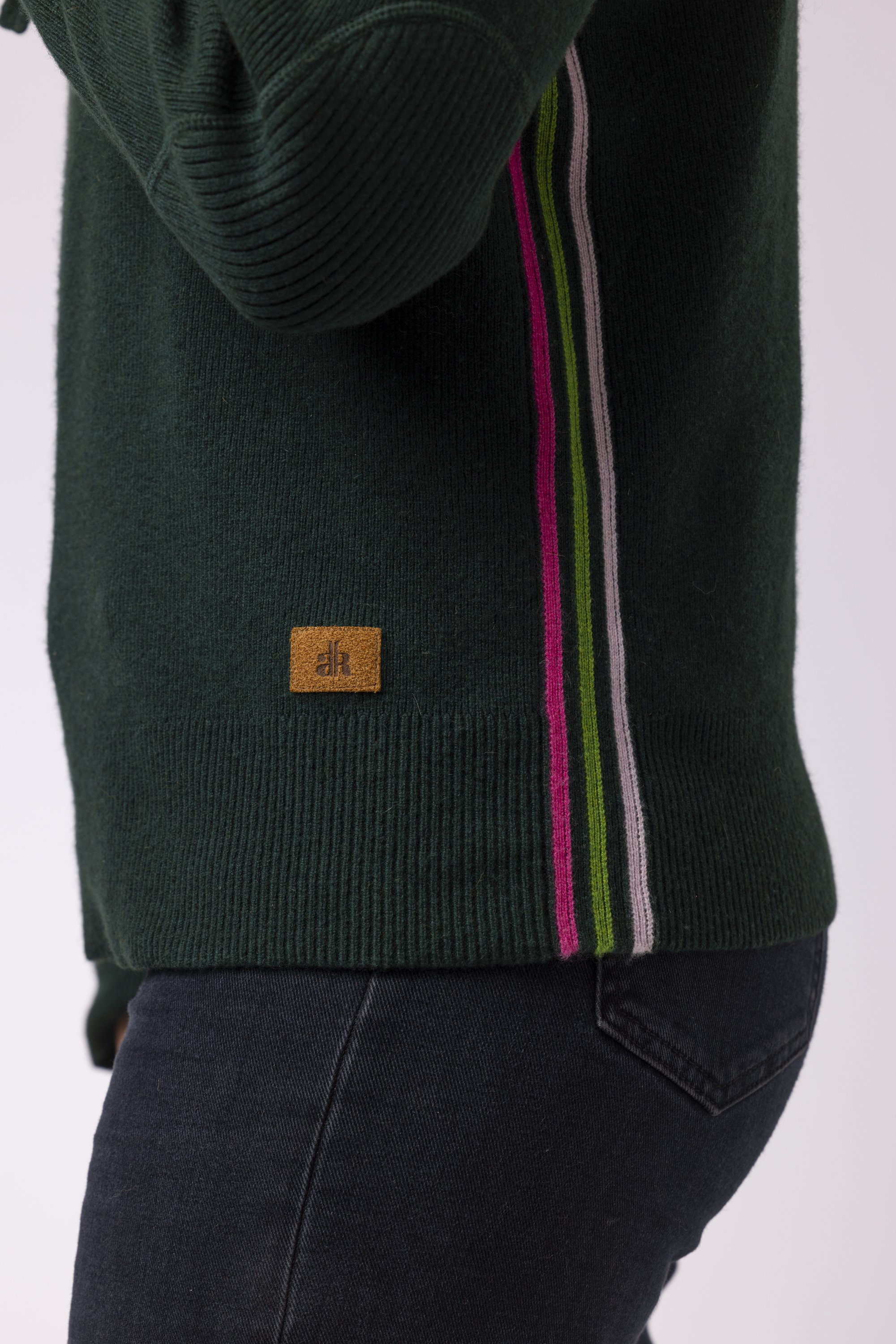 Side view of a woman in a studio wearing a dark green cashmere hoodie with retro stripes on sides