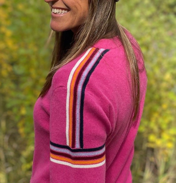 Woman standing outdoors wearing a bright pink crew sweater with retro stripes on sleeves