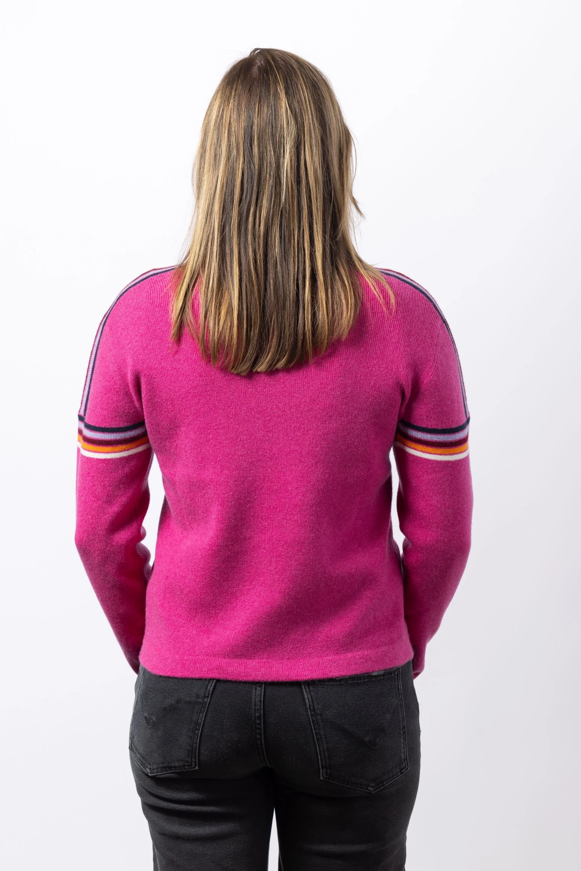 Woman in a studio wearing a bright pink crew sweater with retro stripes on sleeves facing backward
