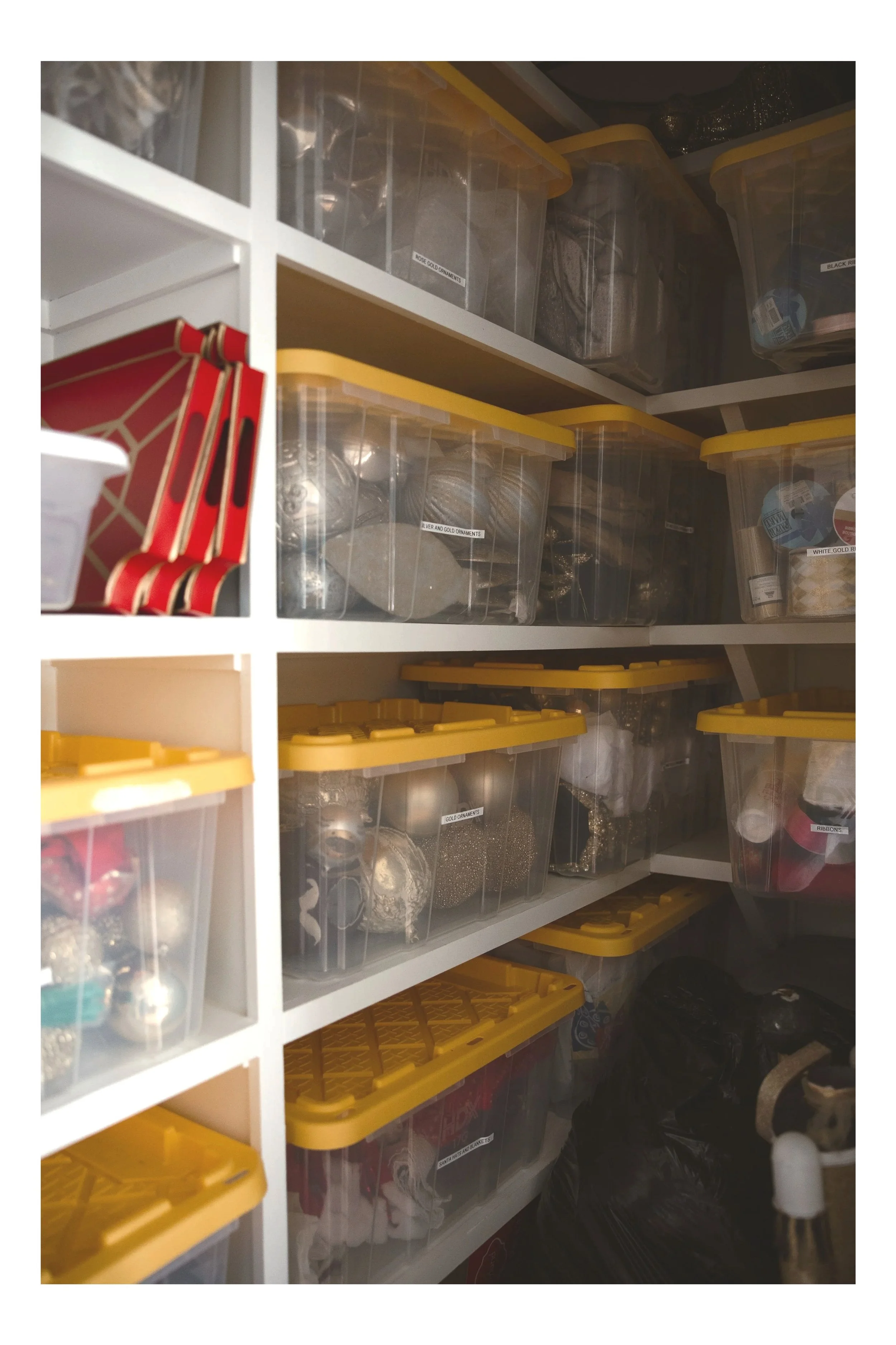 clear bins with yellows lids sitting on a shelf that have labels and are holding christmas decor