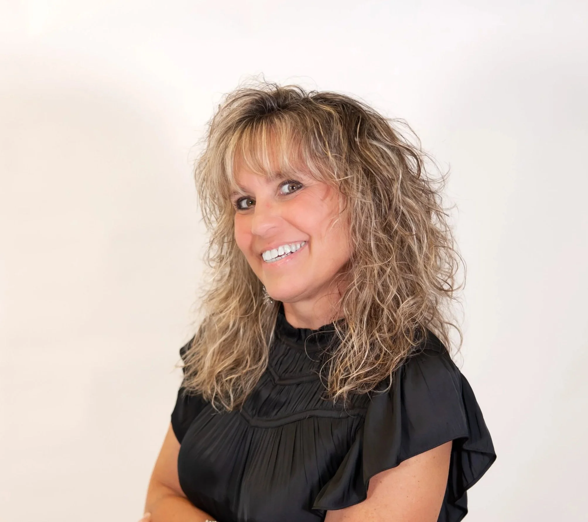 Woman with mid-length blonde hair has arms crossed and is smiling softly