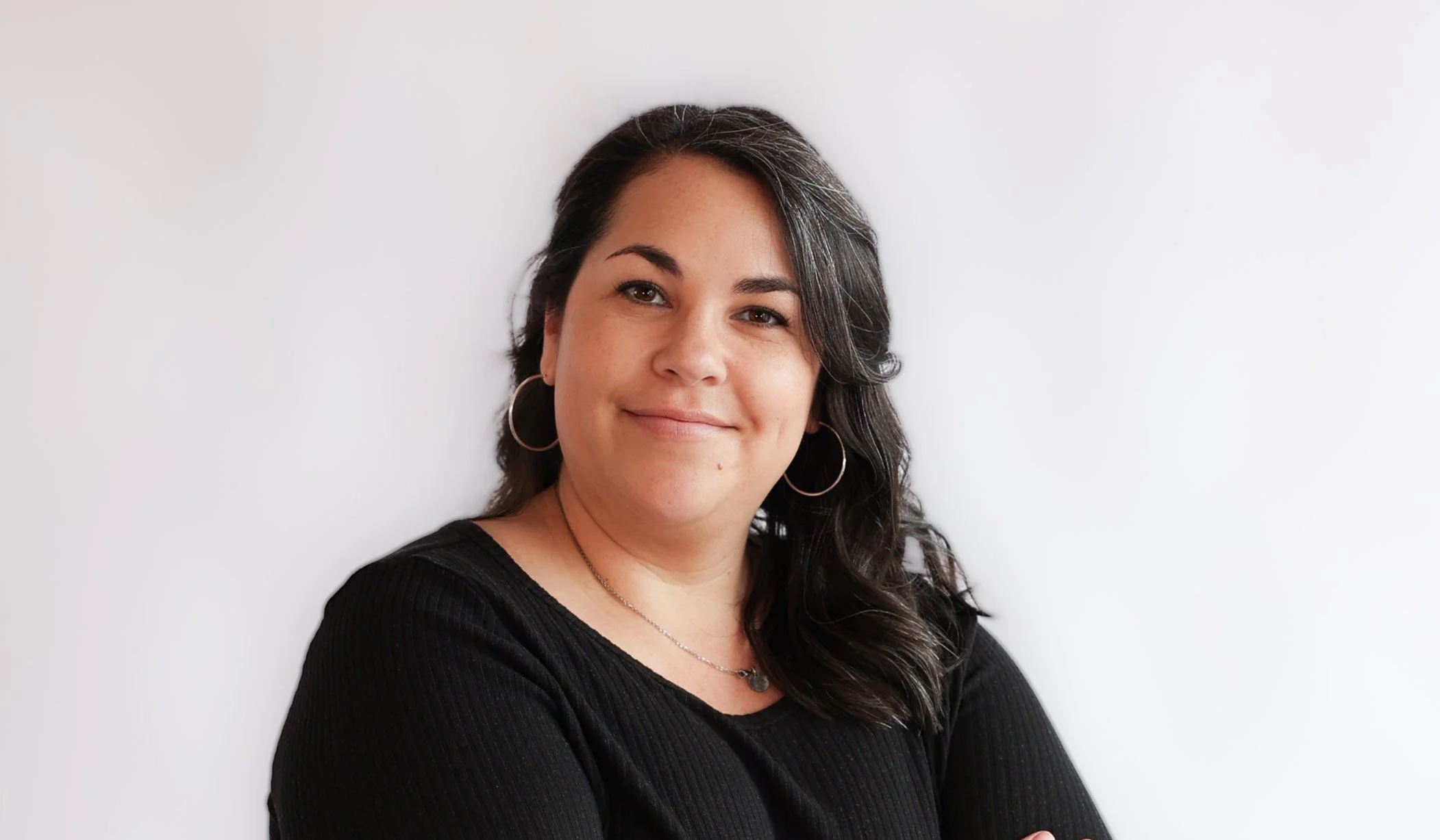 Woman with brown hair hung off to the side and arms crossed is smiling