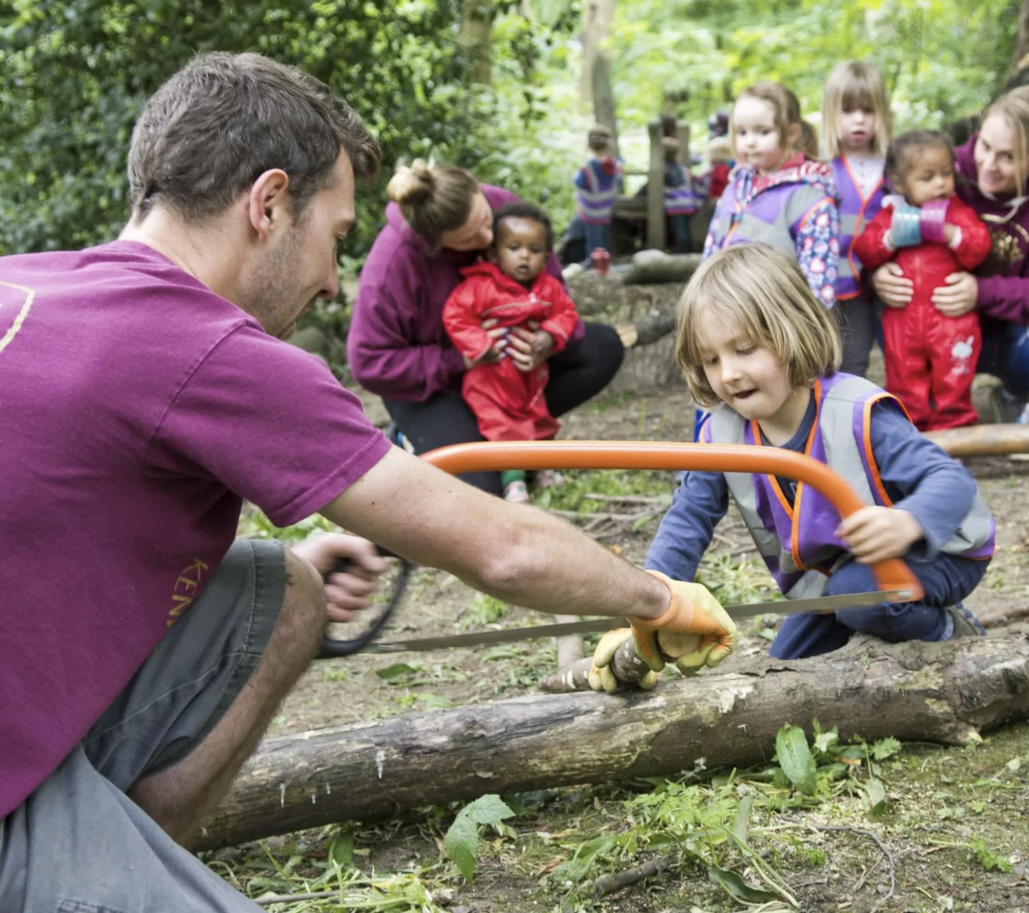 A older child with a teacher learning to cut would while younger children and teachers watch.