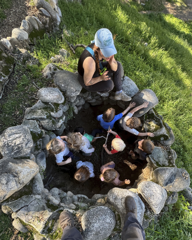 Teacher and preschool children exploring a stone circle outdoors at forest school in Pasadena, California.