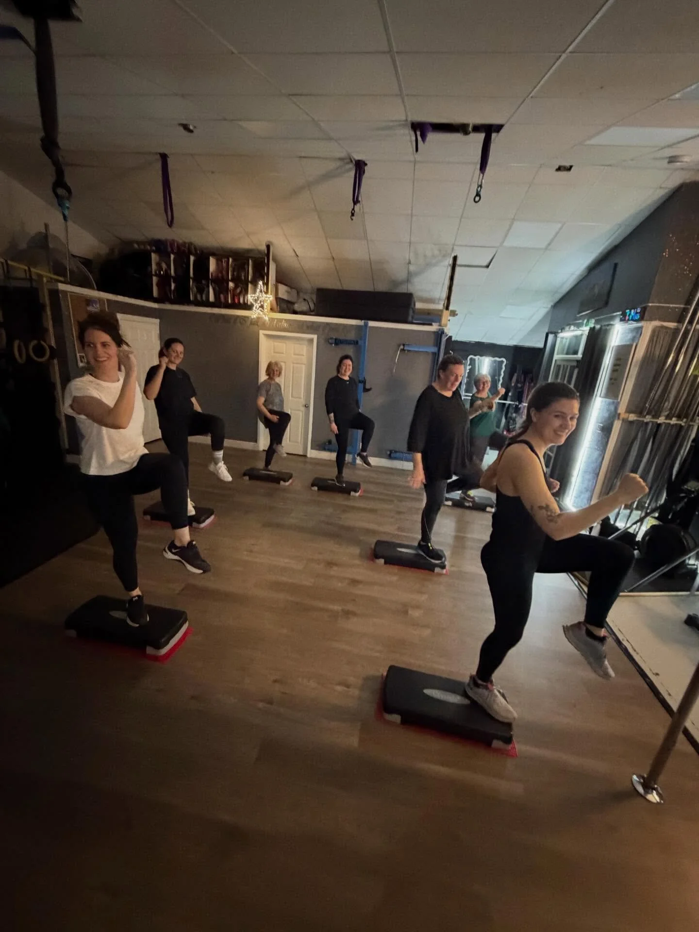 Group of people exercising on aerobic step platforms in a gym studio.
