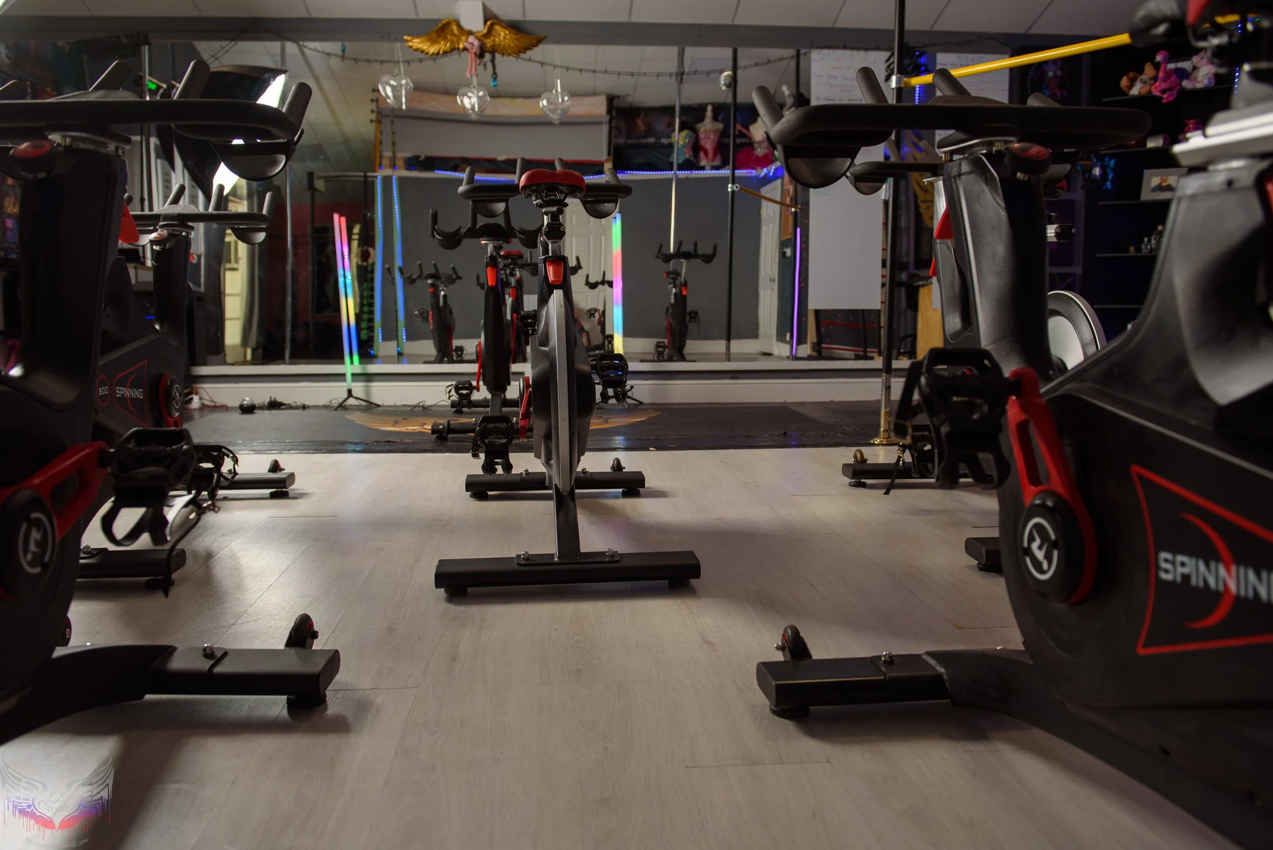 Indoor cycling studio with exercise bikes arranged in rows, mirrors on the wall, and decorative lights and ornaments hanging from the ceiling.