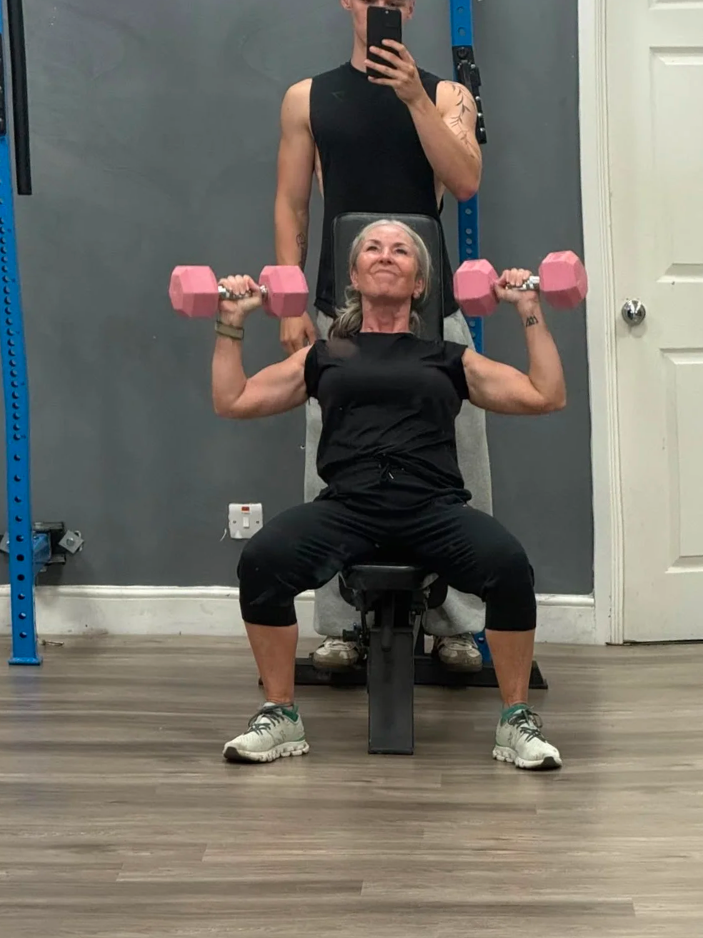 Coach helping with a shoulder press. woman shows visable biceps