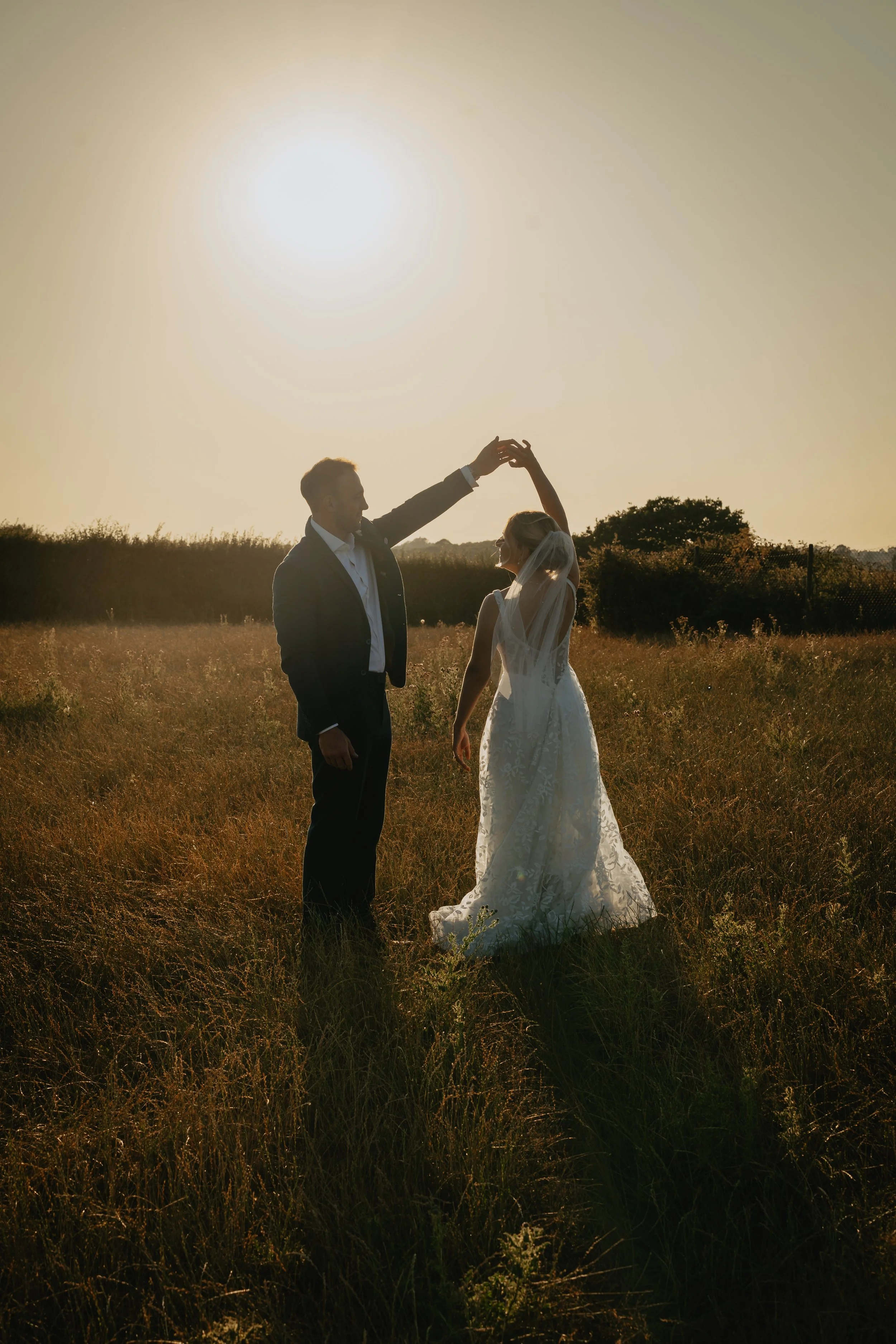 A bride and groom dancing outdoors in a field during sunset.